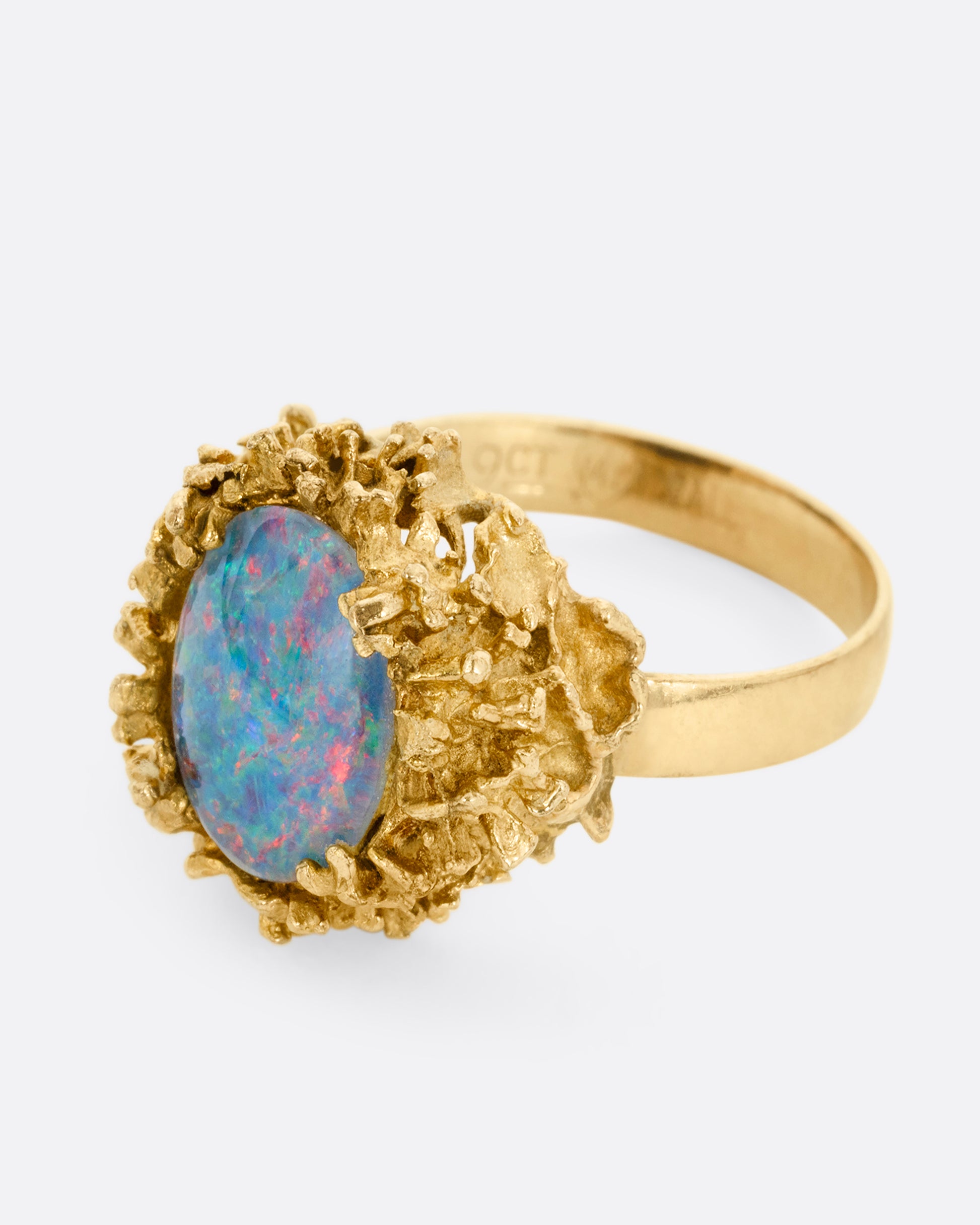 A yellow gold Brutalist era statement ring with an opal doublet in a molten gold nest. Shown from the side.