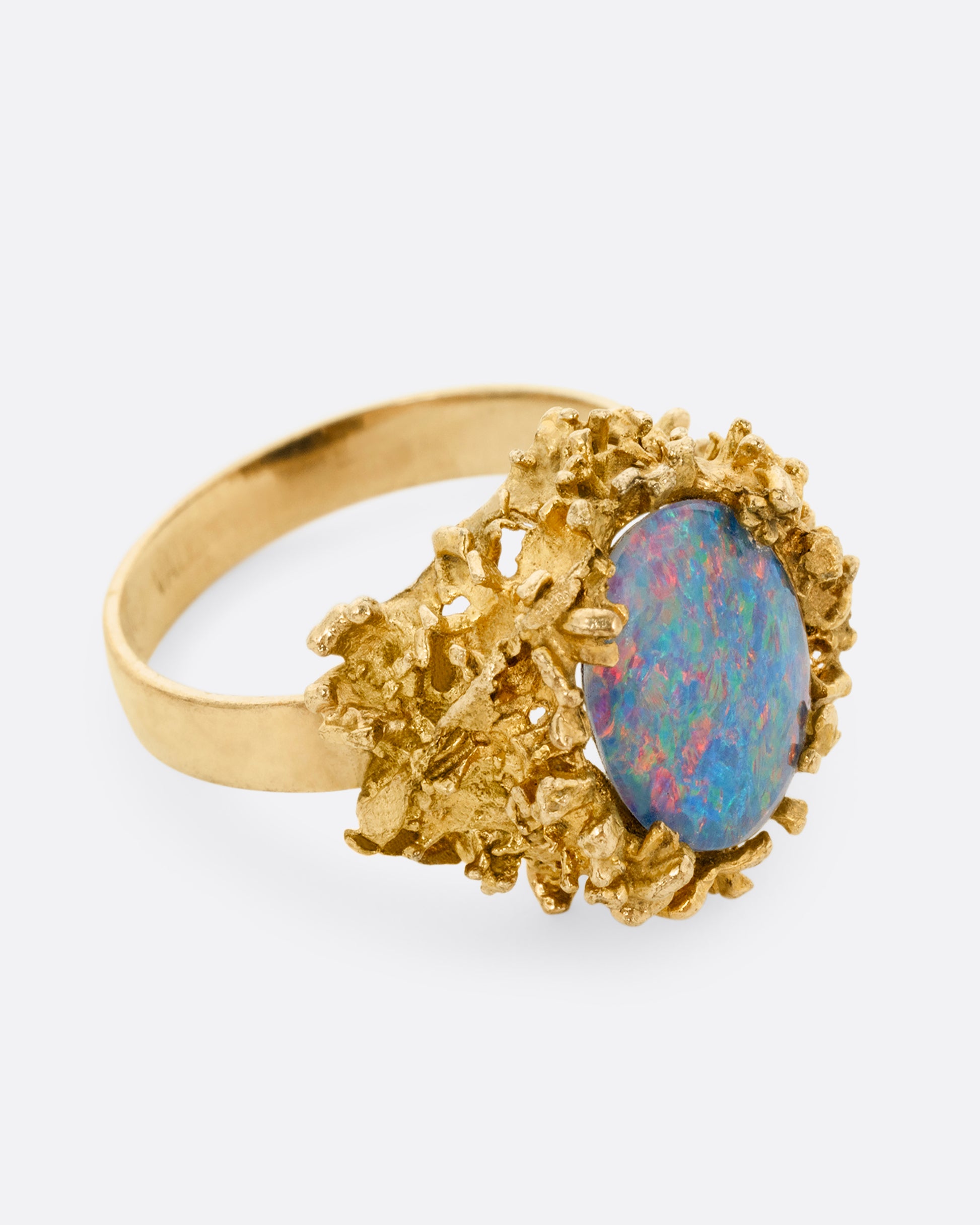 A yellow gold Brutalist era statement ring with an opal doublet in a molten gold nest. Shown from the side.