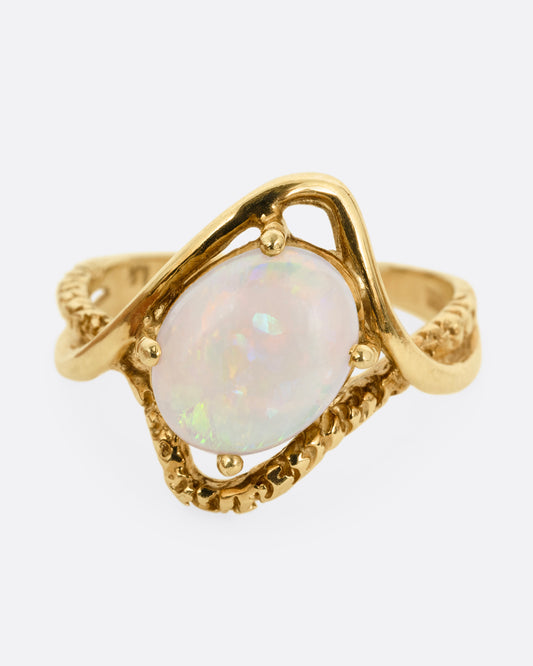 A yellow gold ring with two contrasting bands of polished and textured gold with an oval opal at the center. Shown from the front.