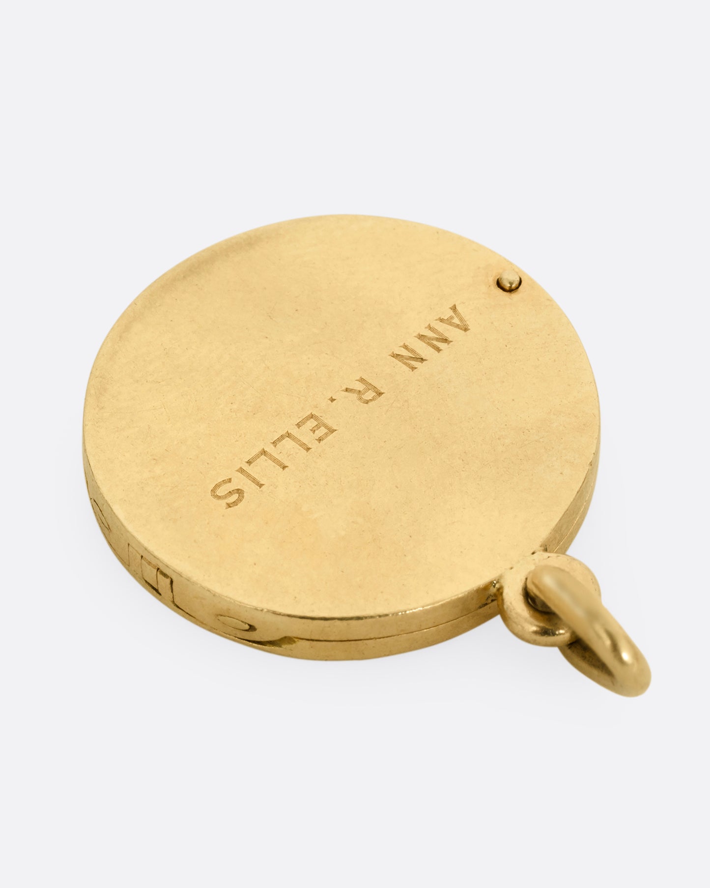 A yellow gold St. Christopher, medallion locket with 'Look at me and be safe' engraved on its edge with a photo frame and a secret slot for a memento on its interior. Shown from the back.