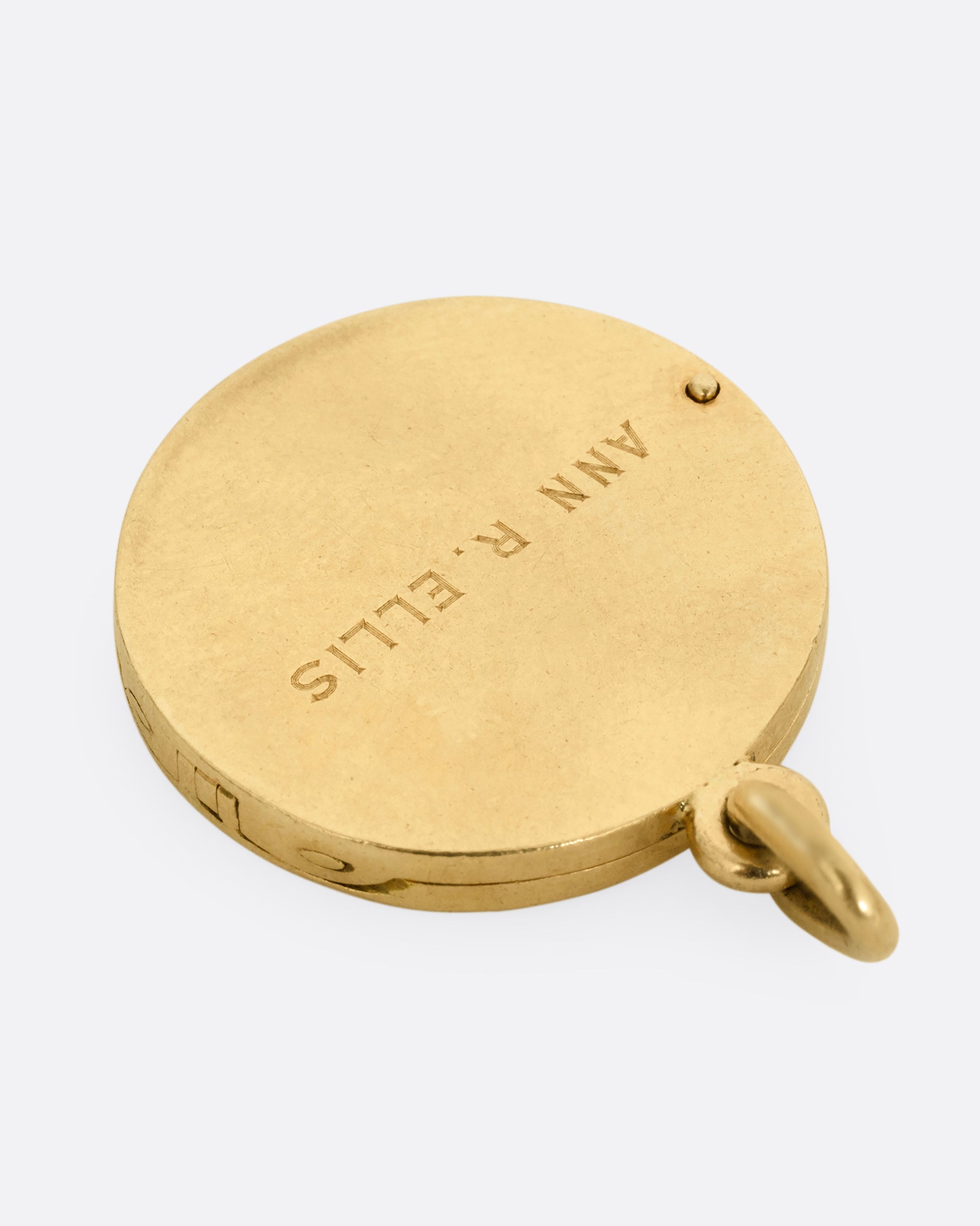 A yellow gold St. Christopher, medallion locket with 'Look at me and be safe' engraved on its edge with a photo frame and a secret slot for a memento on its interior. Shown from the back.