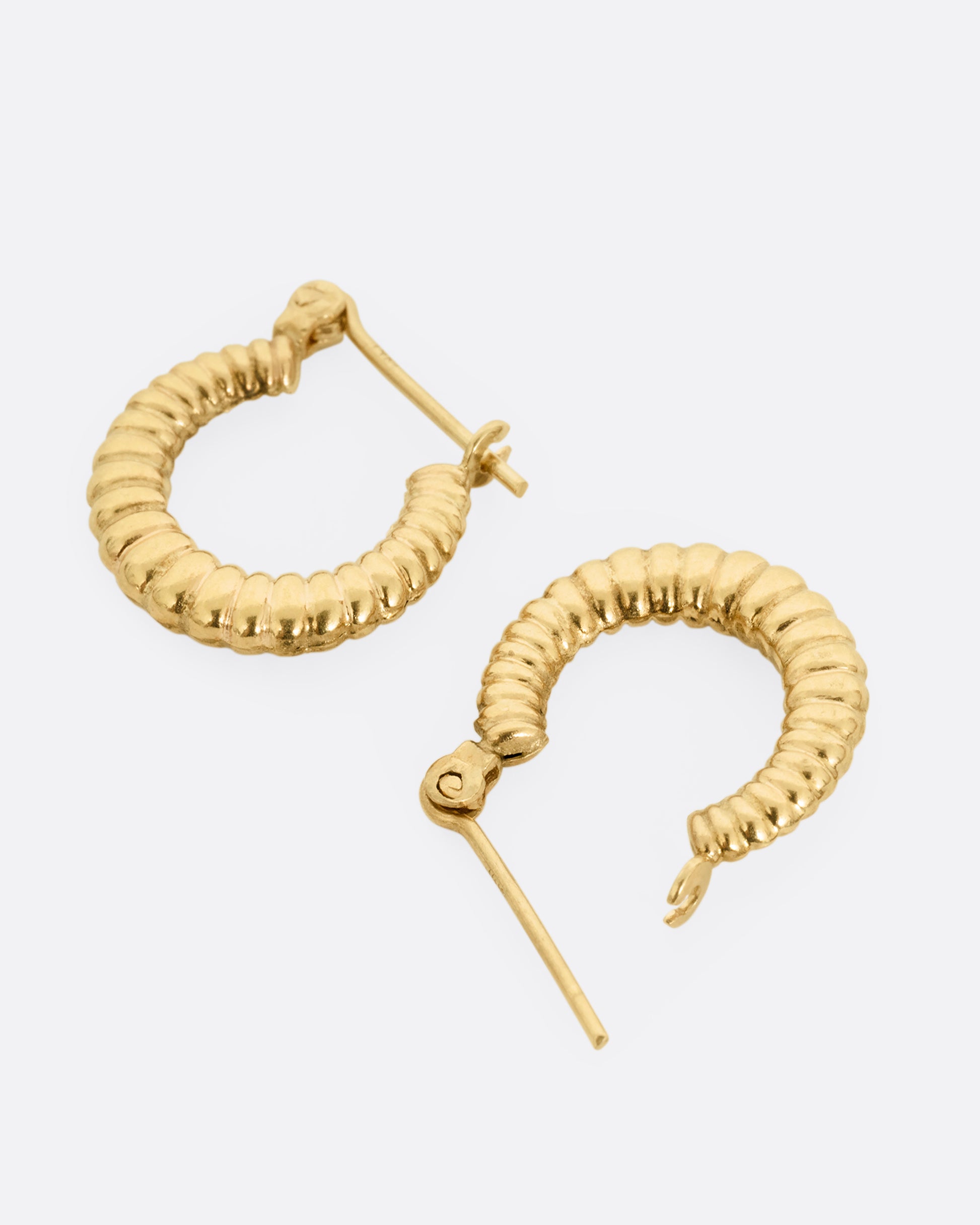A pair of yellow gold ribbed hoop earrings shown lying flat. One earring is open. 