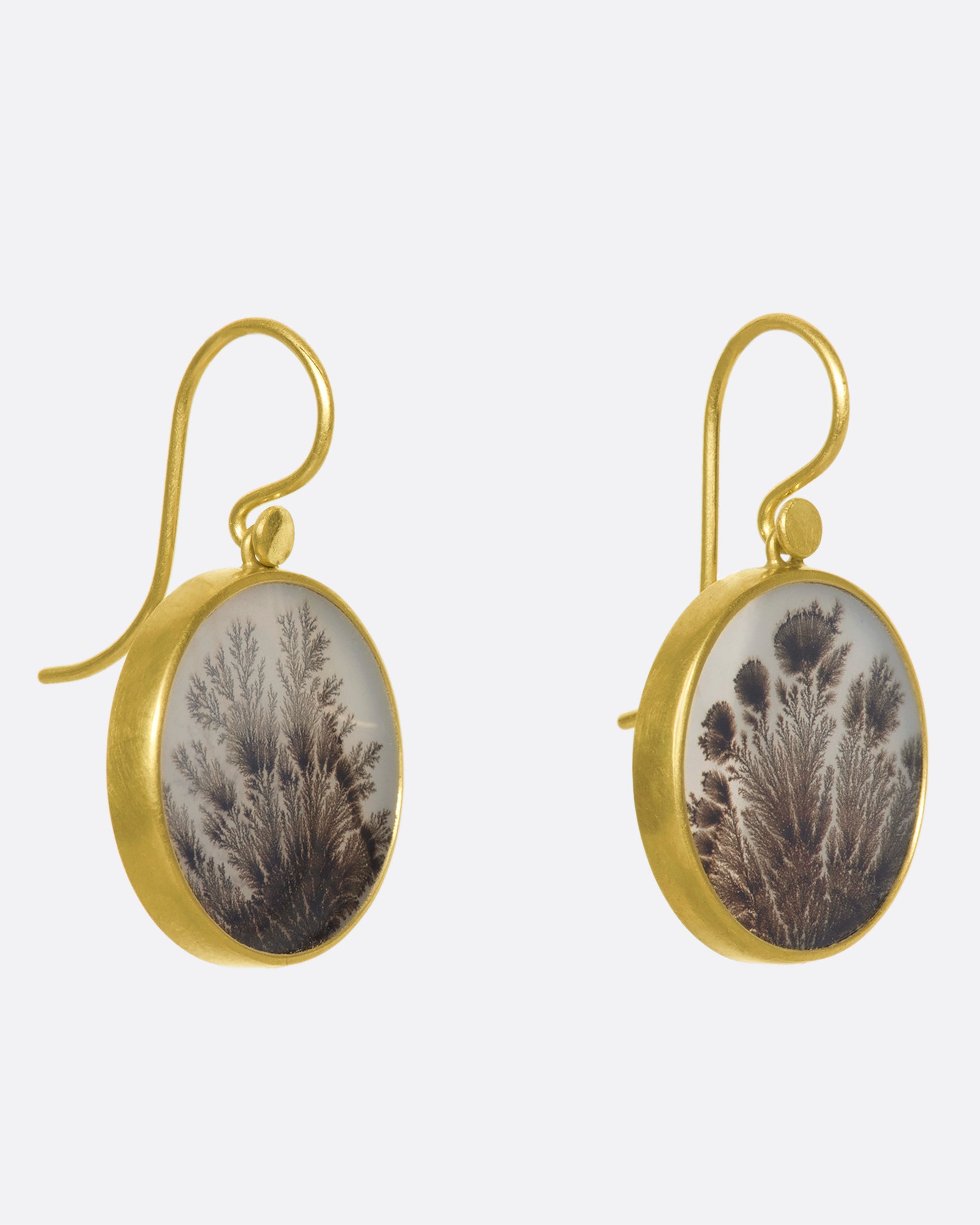 A pair of yellow gold, bezel set, round dendritic agate earrings from the side.