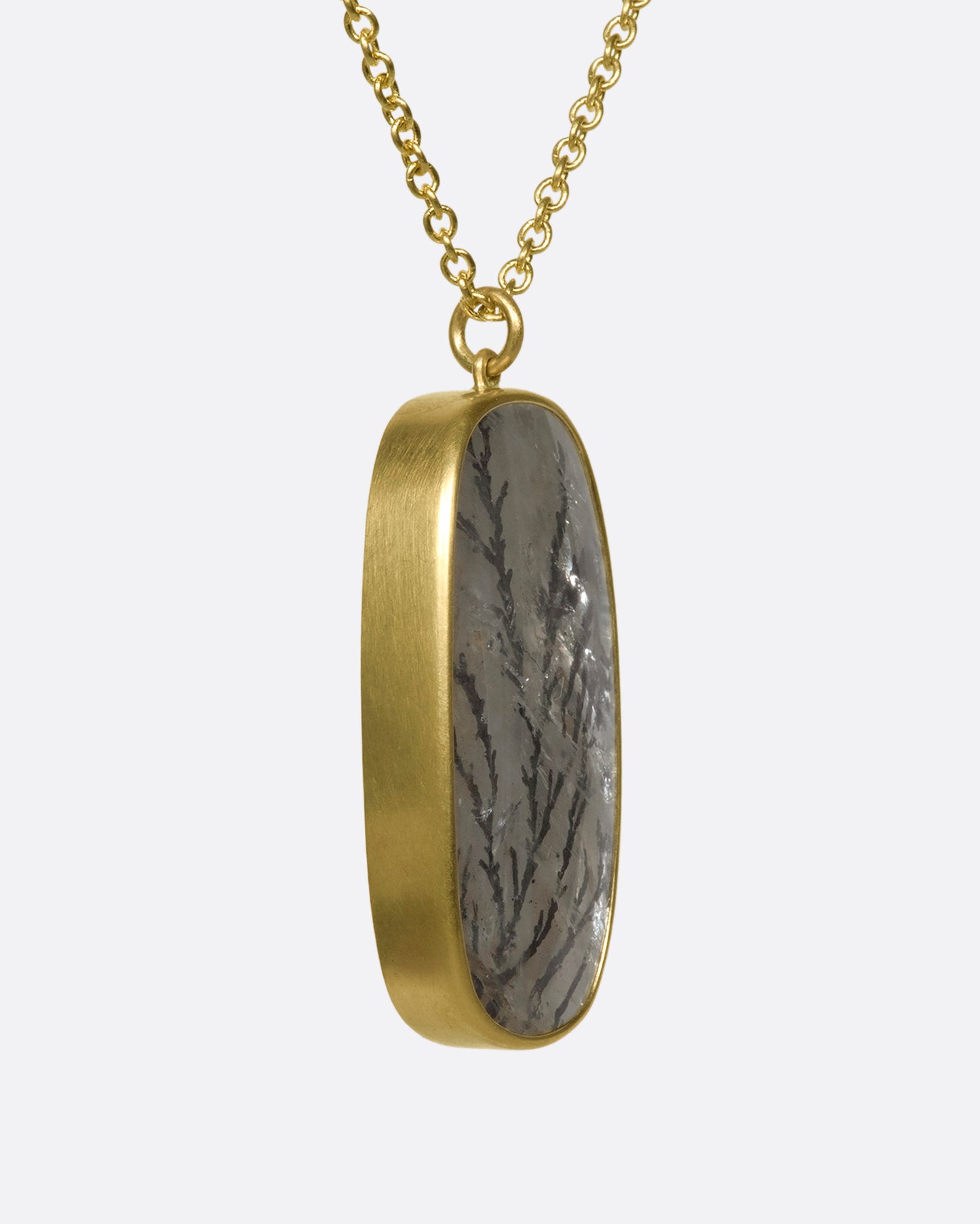 A side view of a hanging dendritic quartz pendant on a yellow gold chain.