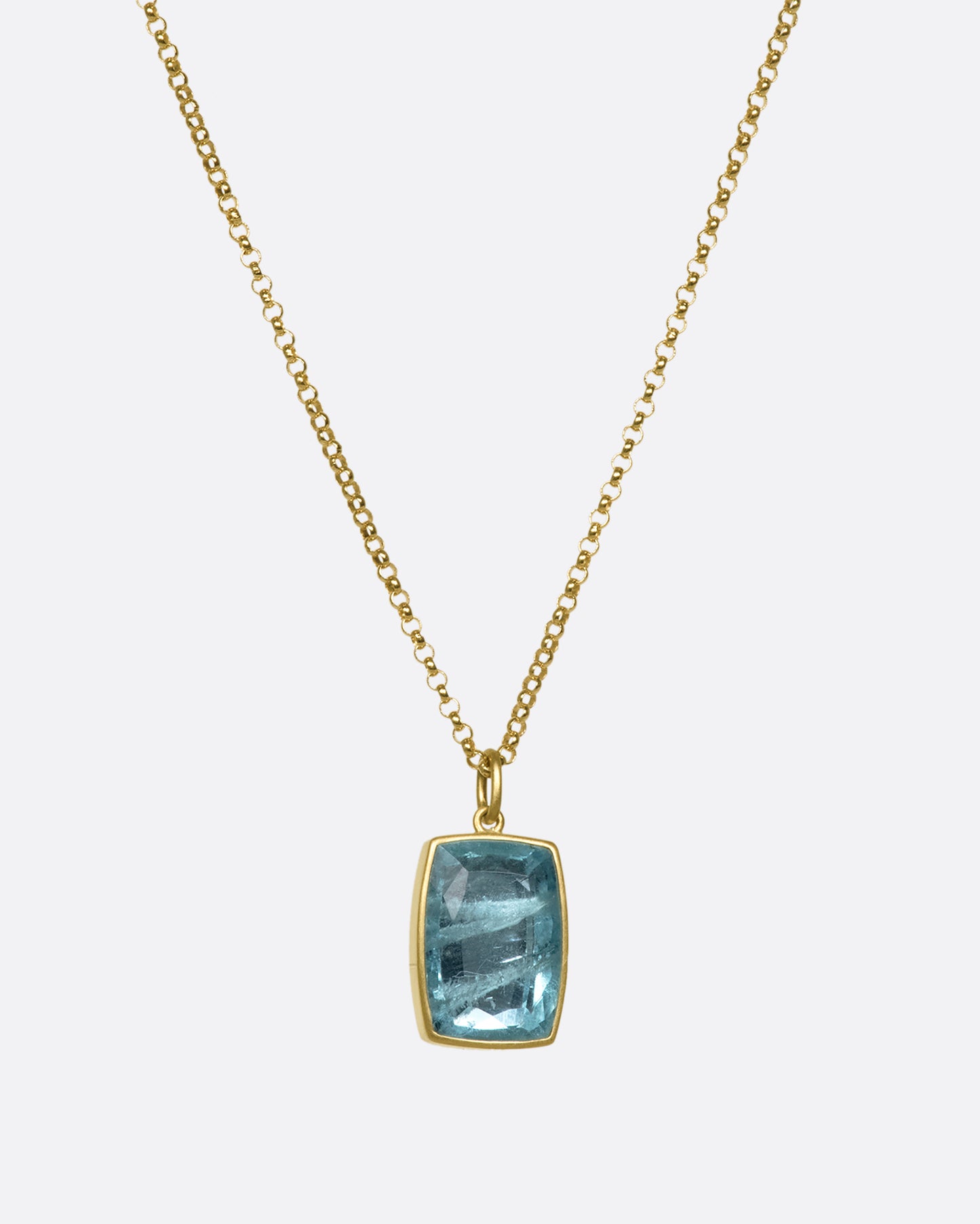 A cushion shaped aquamarine pendant with a yellow gold bezel on a gold chain.