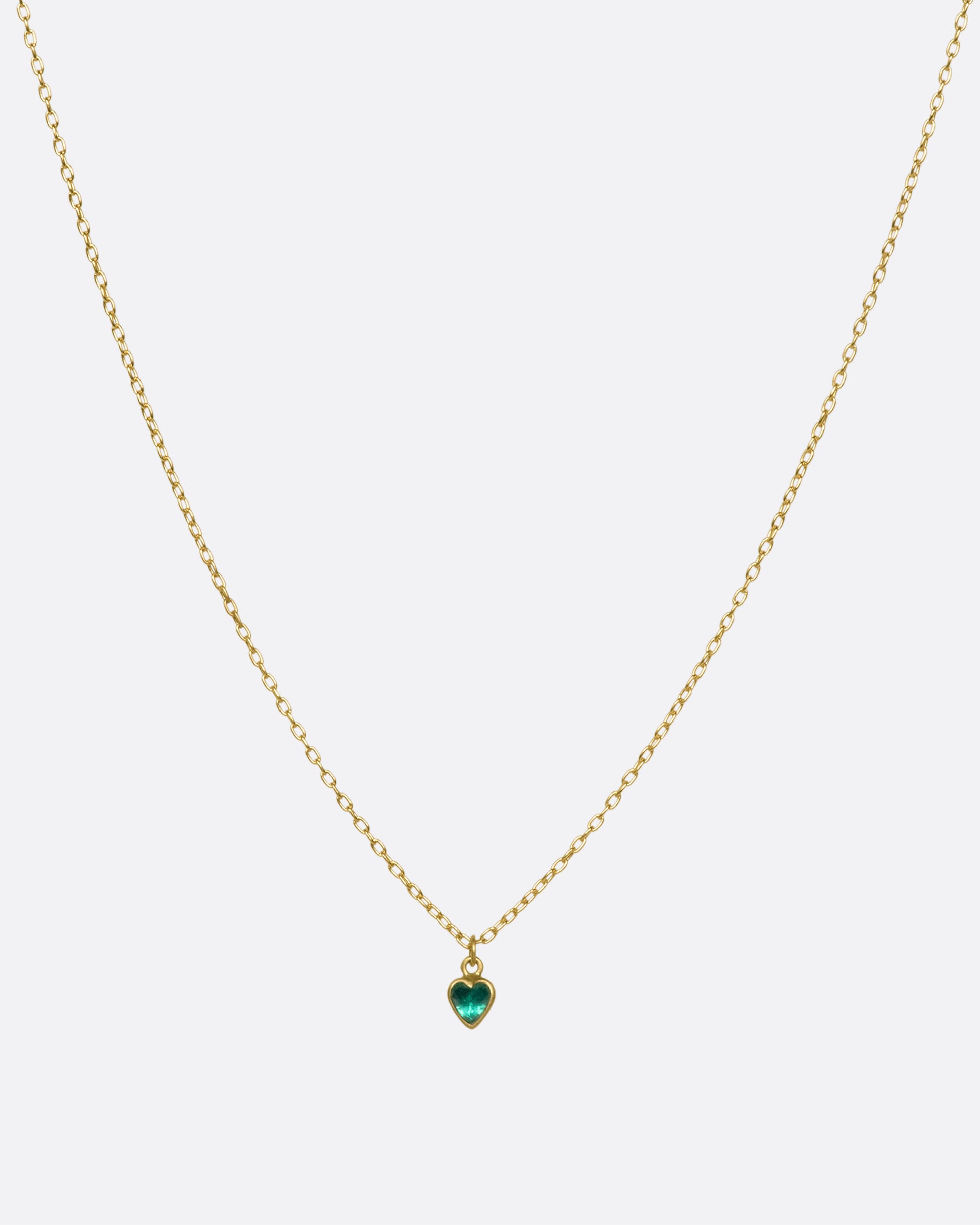 A bezel set emerald heart pendant hanging on a gold chain.