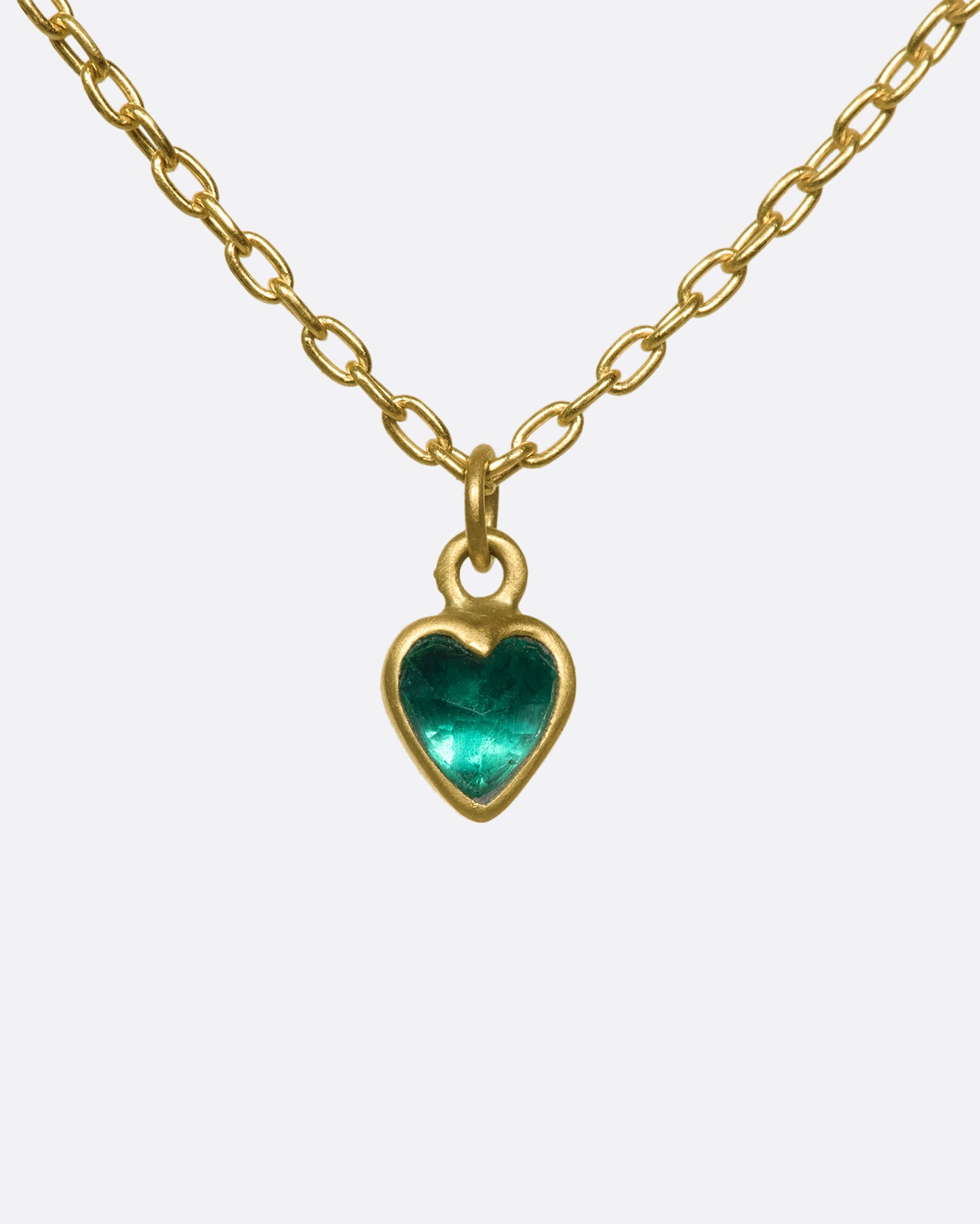 A closeup of a bezel set emerald heart pendant hanging on a gold chain.