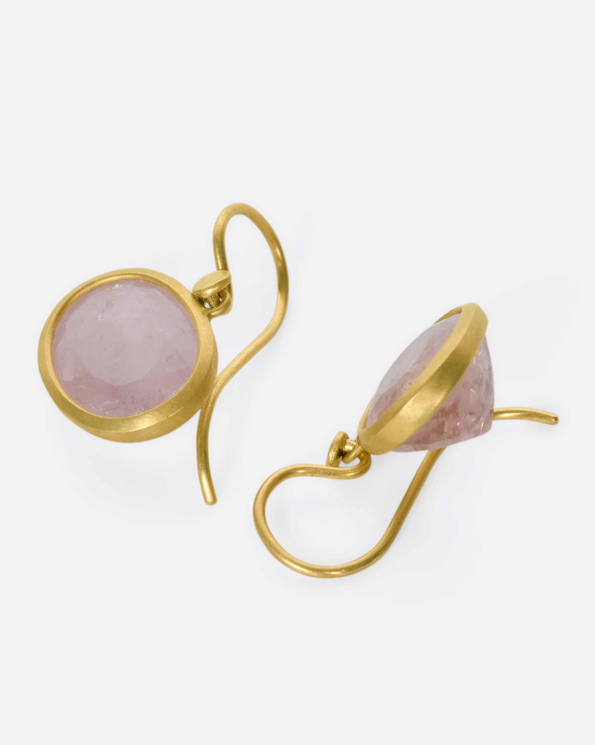 A pair of oval morganite drop earrings with yellow gold bezels and hooks lying down.