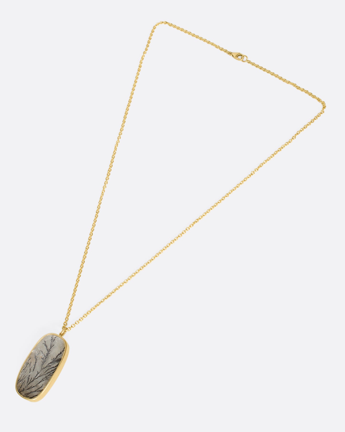 An overhead view of a dendritic quartz pendant on a yellow gold chain laying down flat.