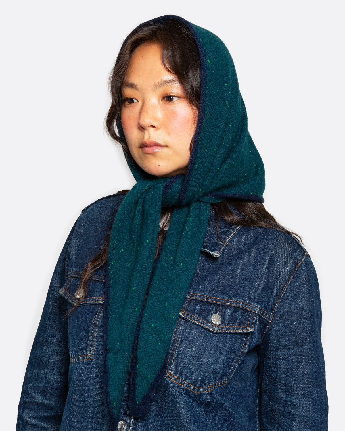A dark teal green ribbed knit scarf with tiny bright green flecks, and a navy striped border, shown tied from the front on a person.