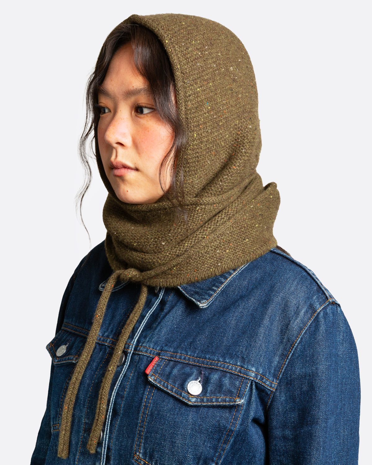 A donegal flecked olive hooded scarf with elongated sides, shown wrapped on a person.