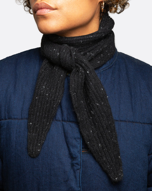 A black ribbed knit scarf with tiny flecks, shown wrapped and tied from the front on a person.