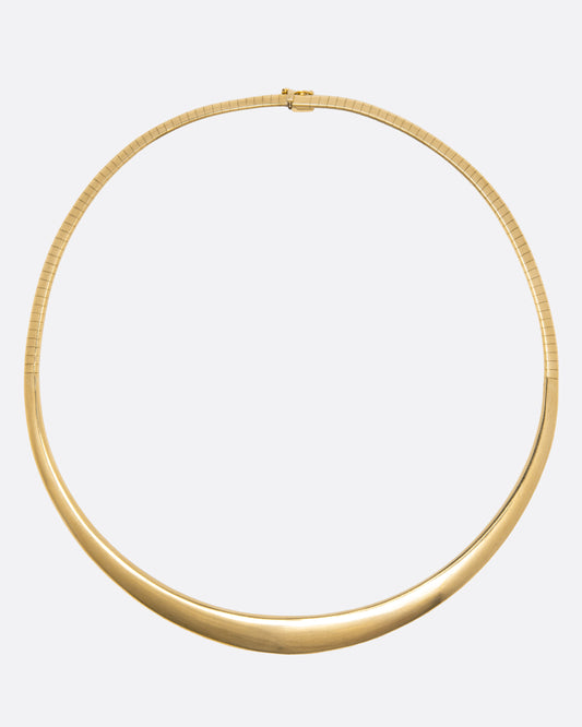 A yellow gold collar necklace with graduated width and a safety closure, shown from above laying flat.