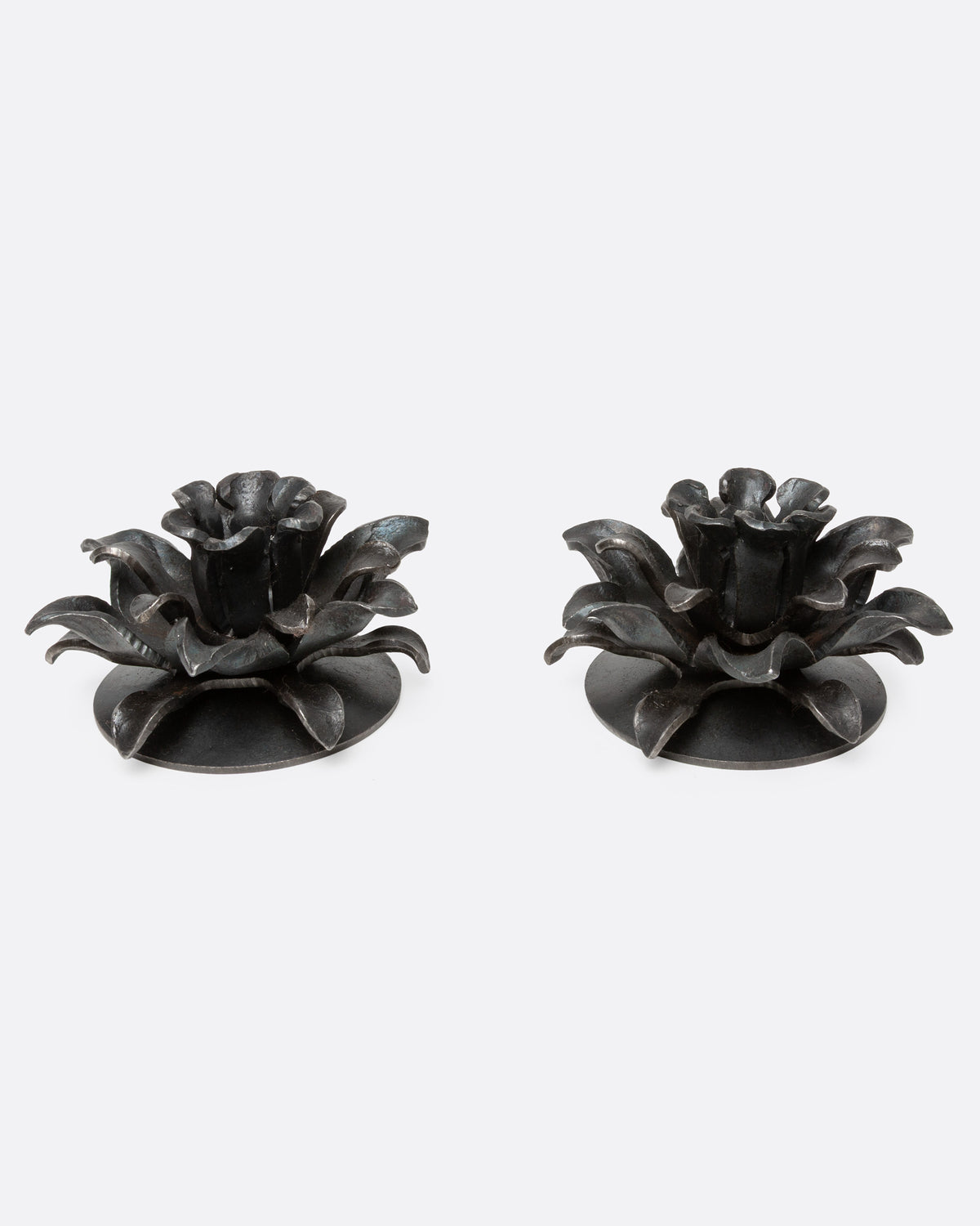 A pair of iron candle holders shaped like stylized flowers, shown from the front.
