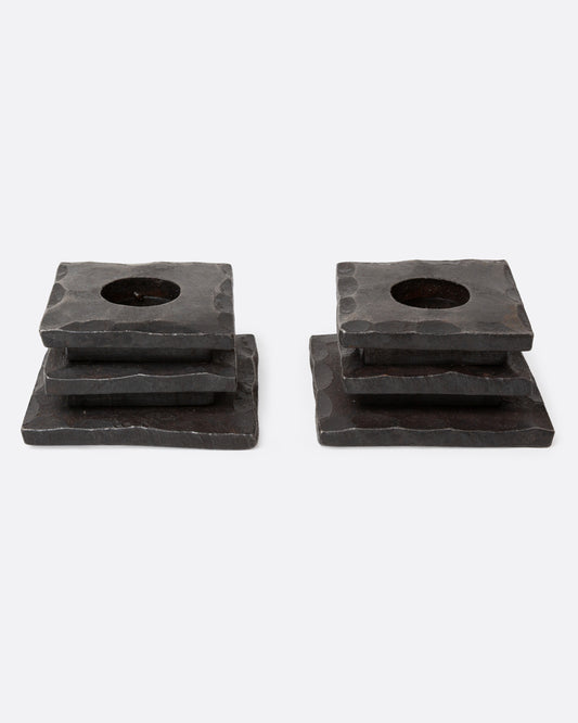 A pair of iron stacked square candle holders with a hammered texture and a circular cutout in the top surface, shown from the front.