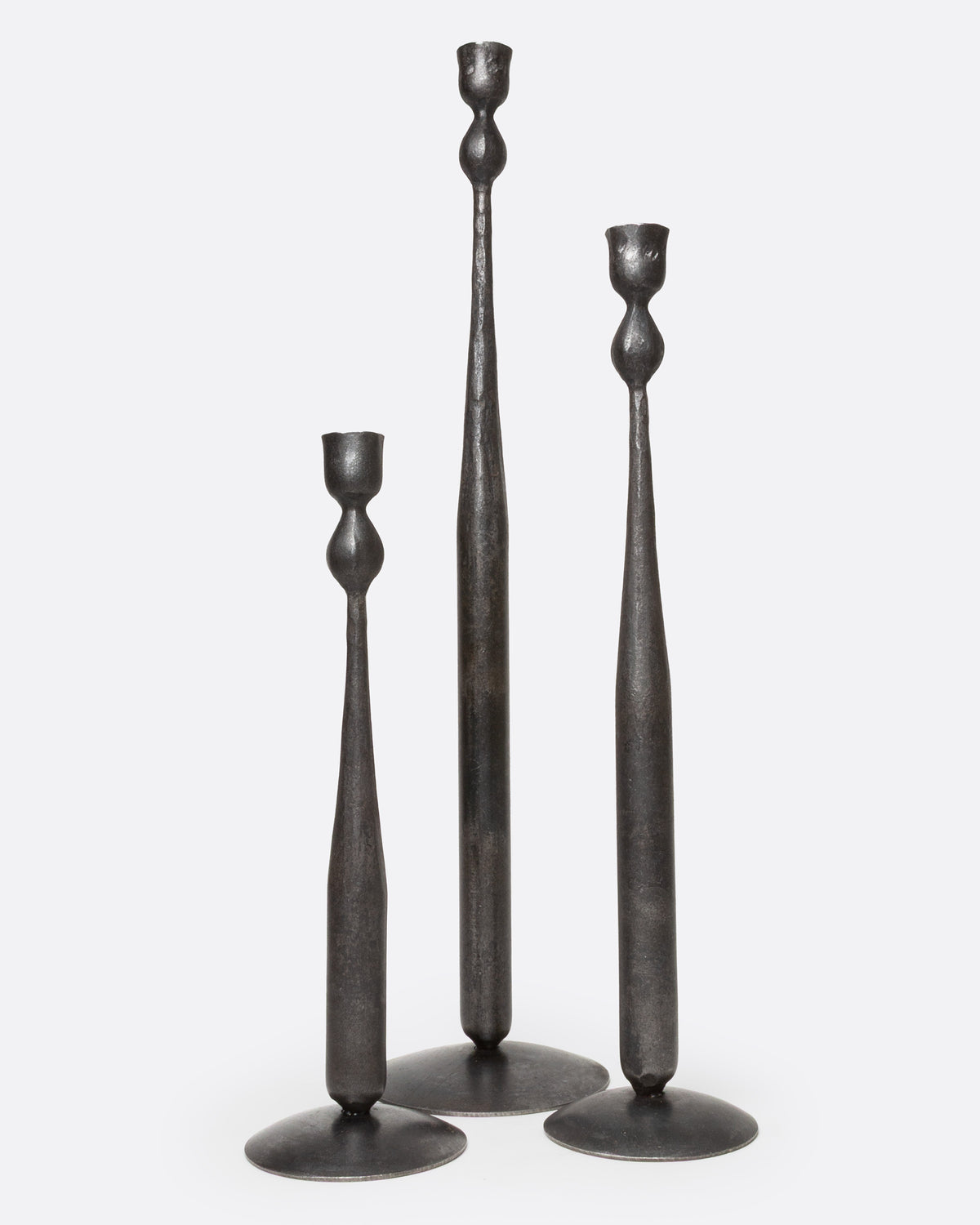 Three tall, slender iron candlestick holders in three different sizes, with flared circular bases, shown from the front.