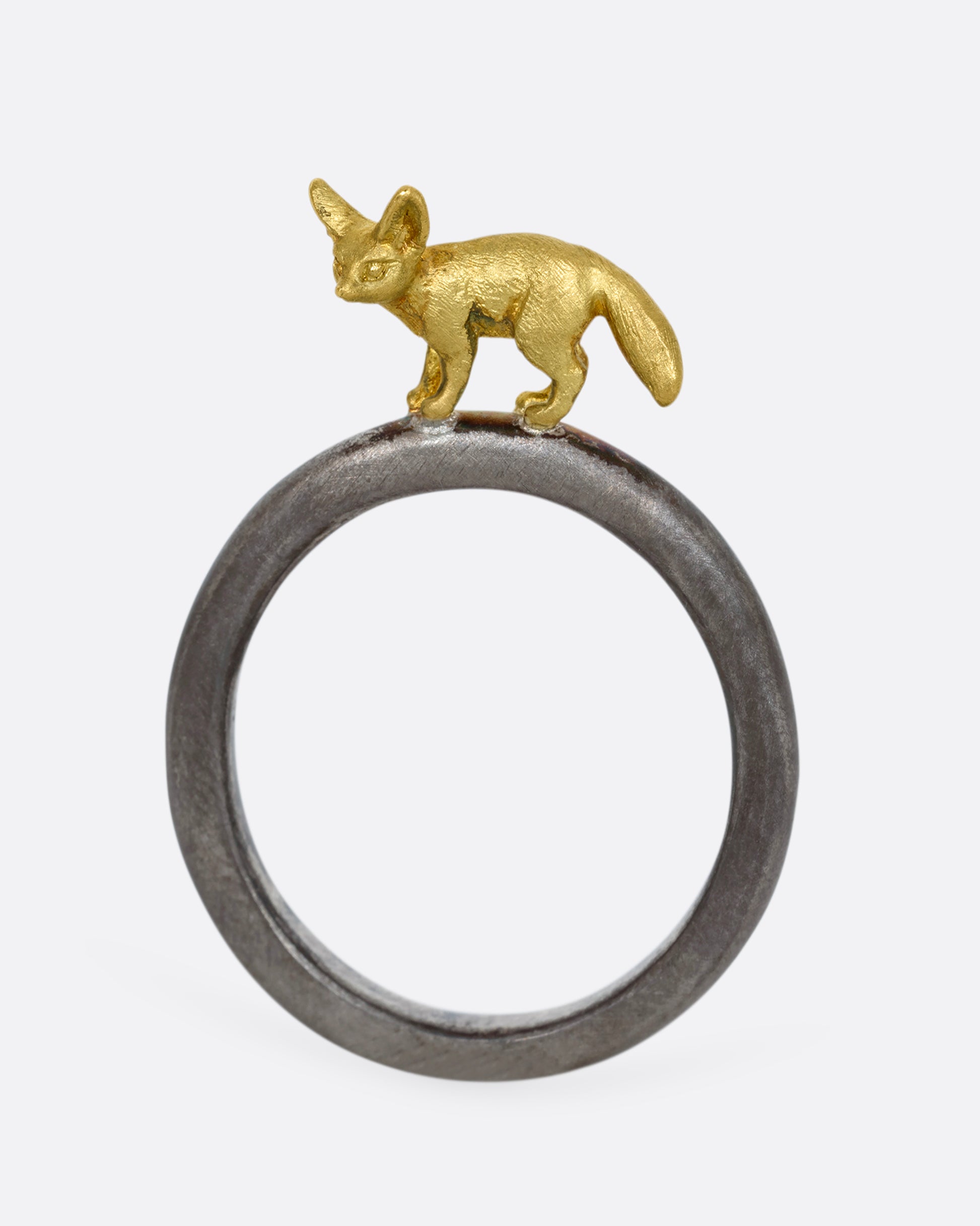 A sterling silver ring with a yellow gold fennec fox standing on the band. Shown standing up, from the front.