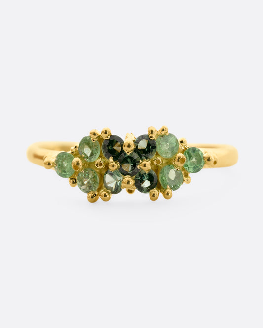 A yellow gold ring with a cluster of eleven green sapphires and tsavorite. Shown from the front.