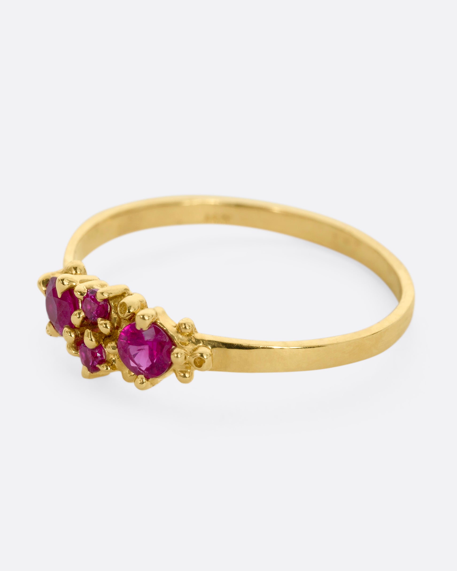 A yellow gold ring with a cluster of four rubies. Shown from the side.