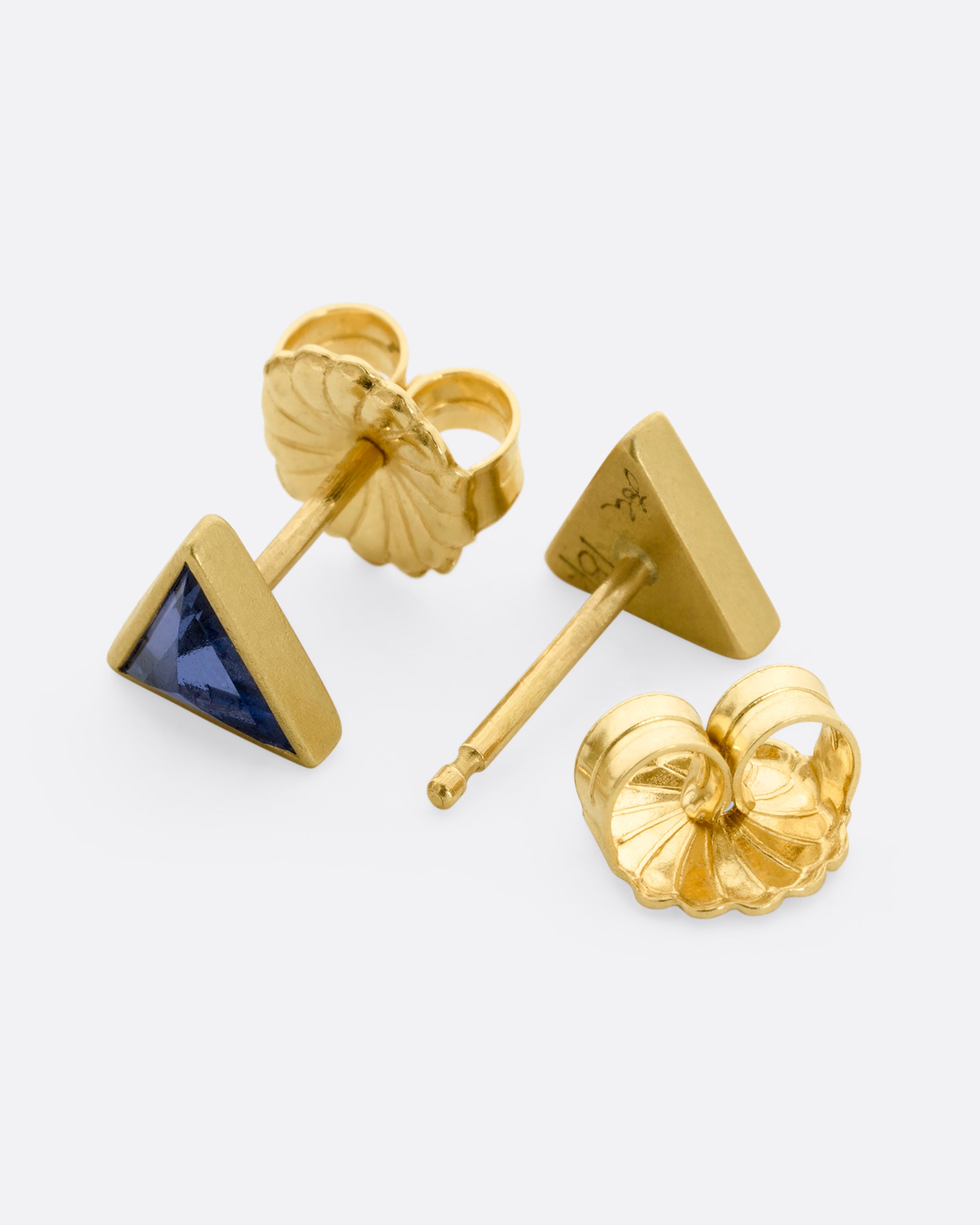 A pair of yellow gold triangle studs with pale blue bezel set sapphires. View from the front and back, alternating.