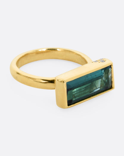 A yellow gold ring with a baguette indicolite tourmaline and small white diamonds. Shown from the alternate side.