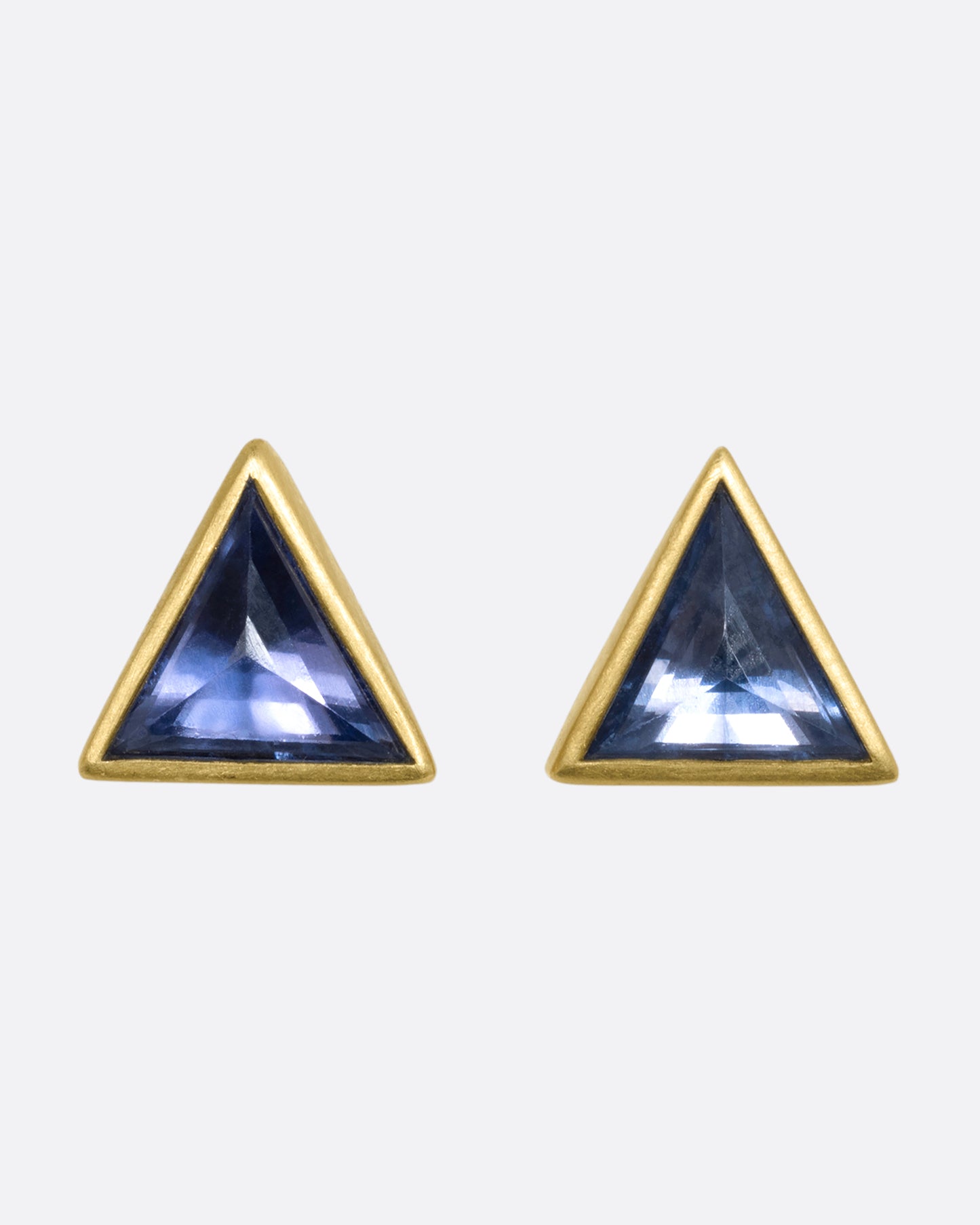 A pair of yellow gold triangle studs with pale blue bezel set sapphires. View from the front.