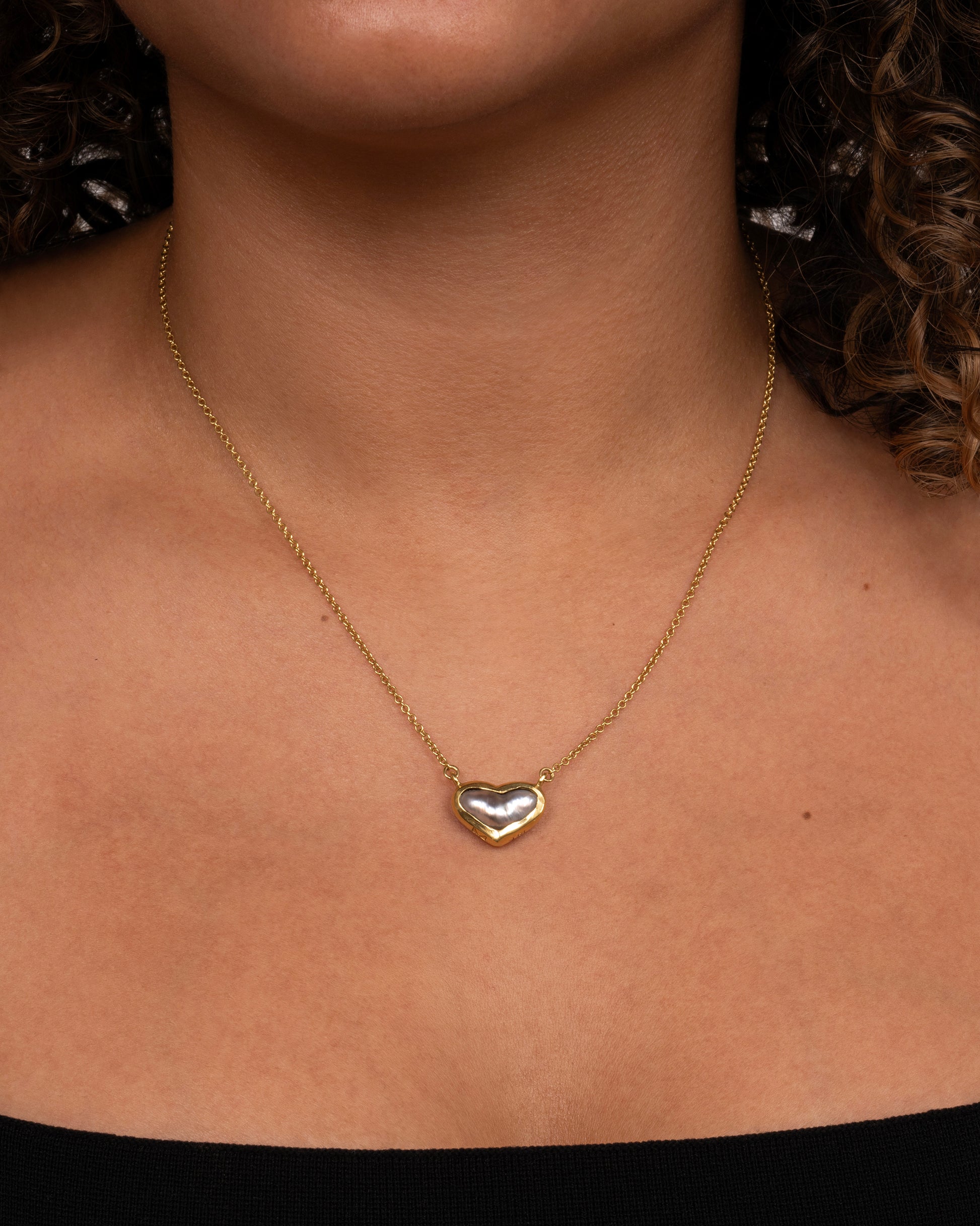 yellow gold necklace with a heart shaped pearl shown worn around he neck