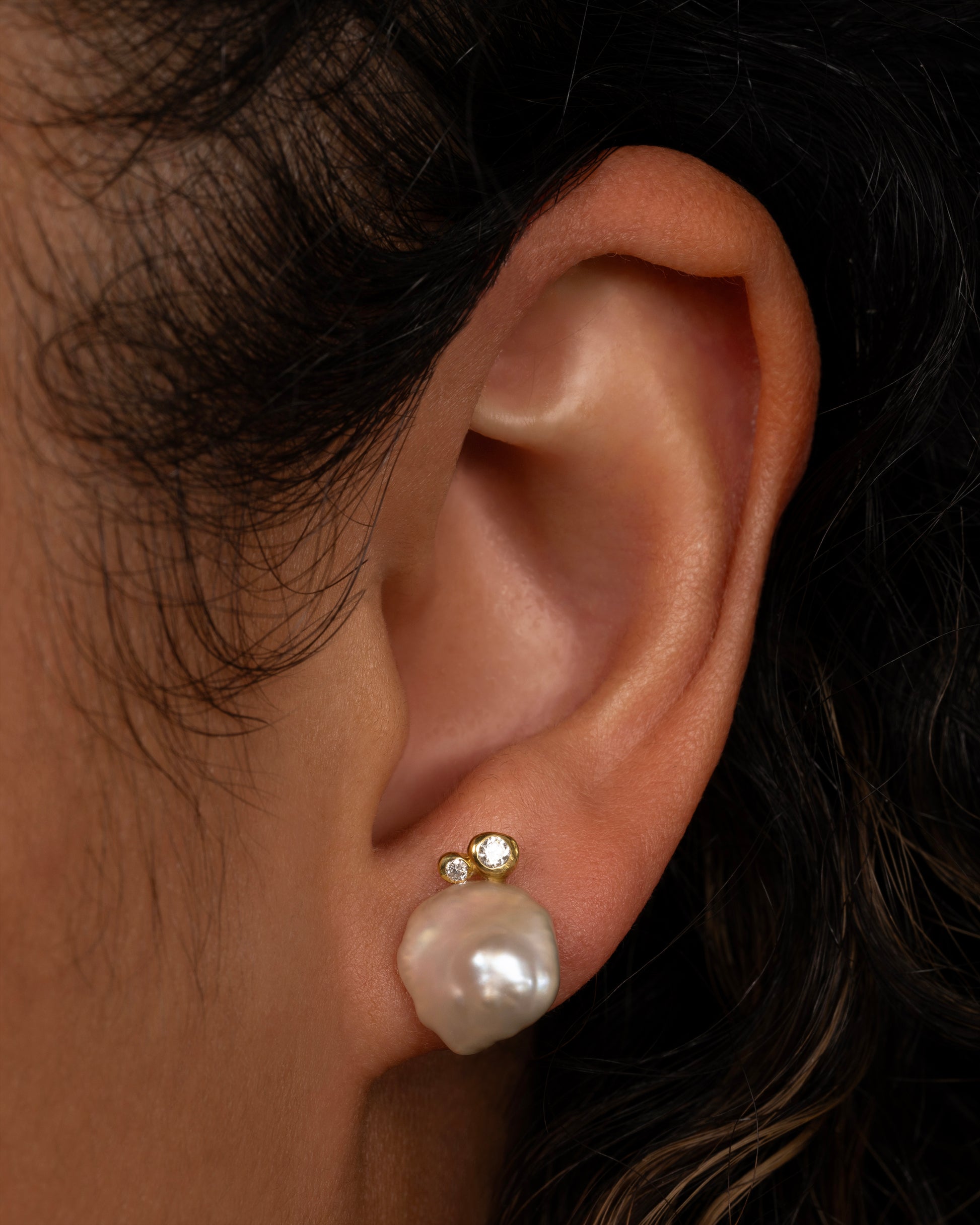 A pair of yellow gold studs with Keshi pearls and white diamonds. Shown on an ear.