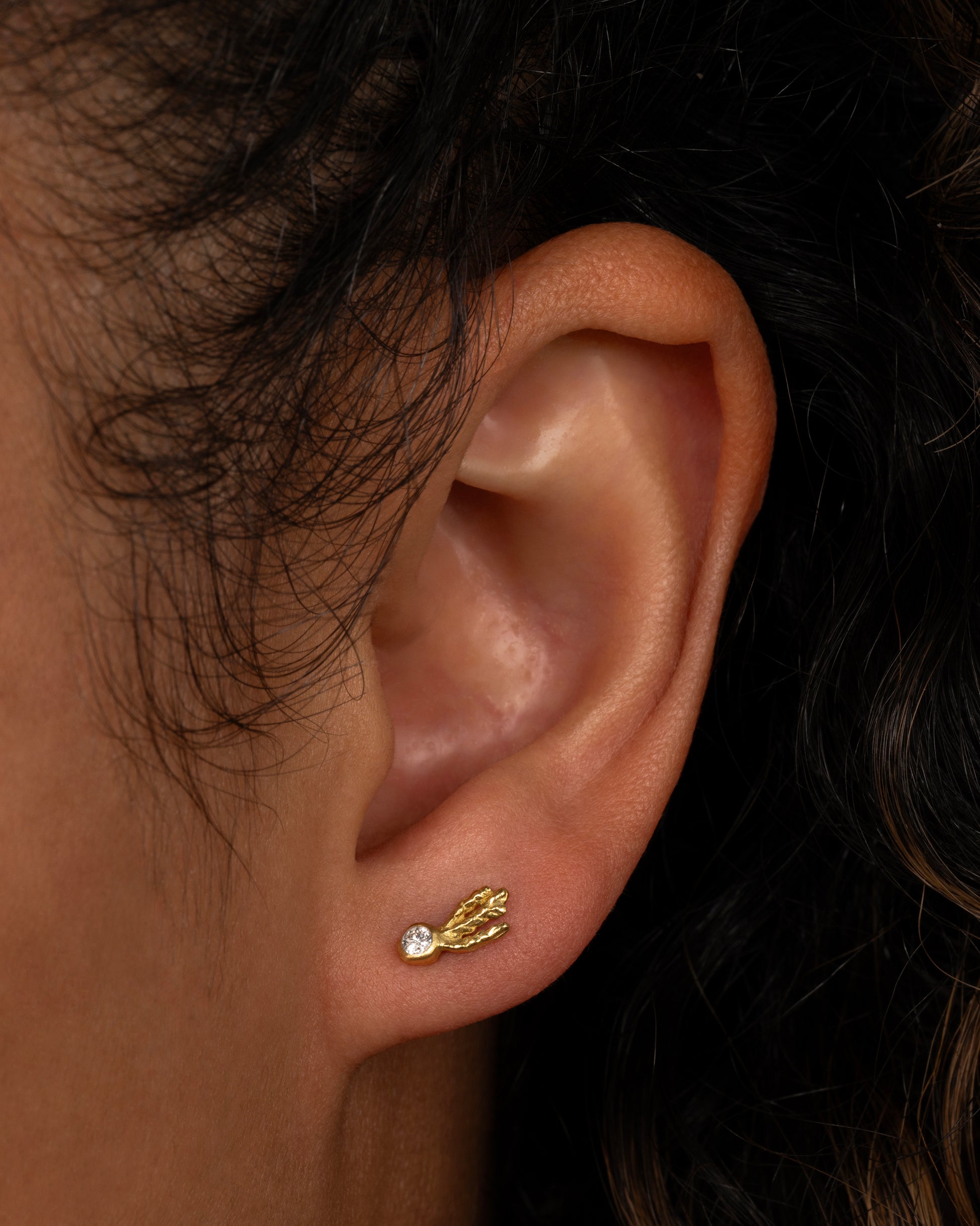 18k gold and diamond stud earrings that look like glowing sea creatures swimming across your ear. Shown on an ear.