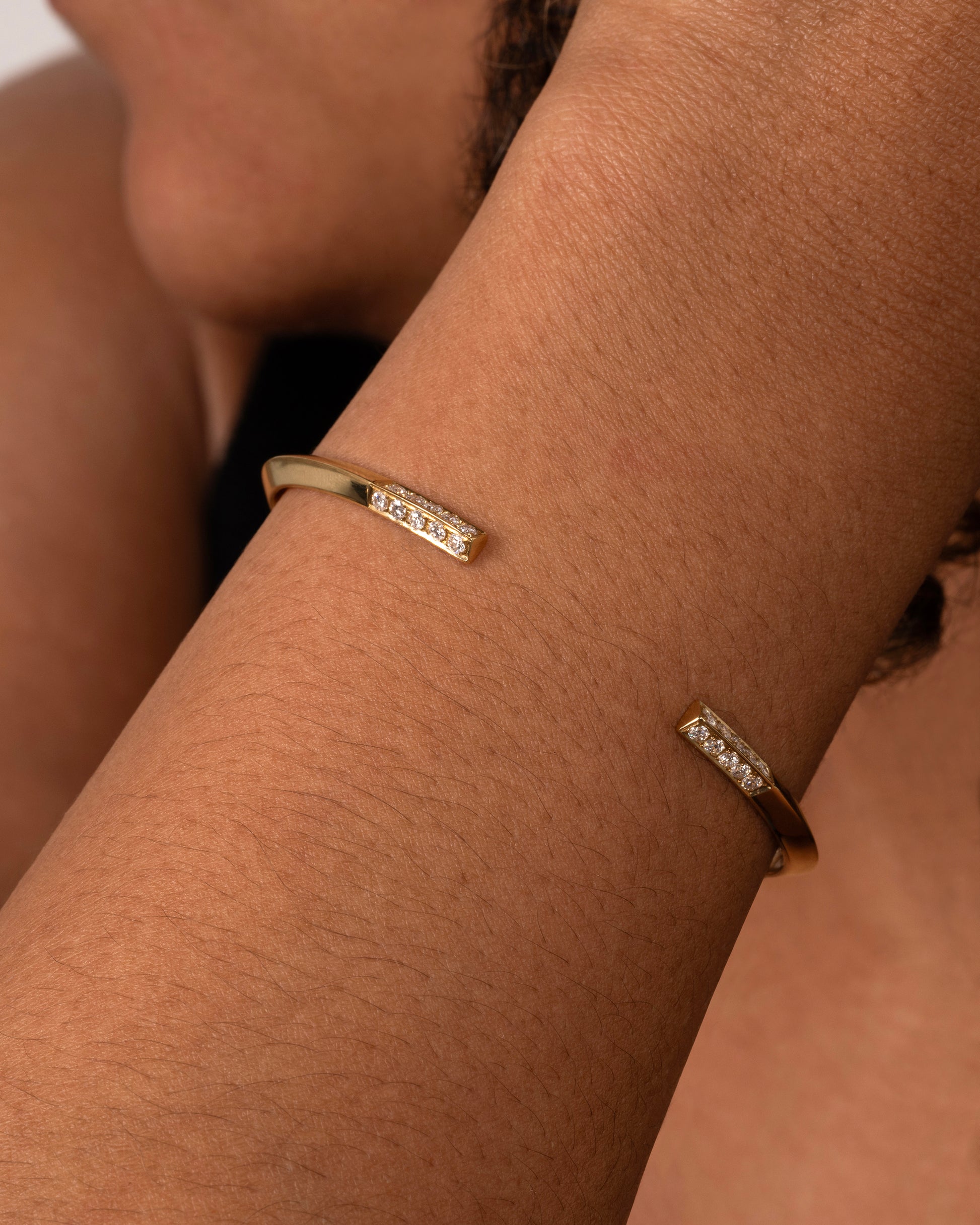 A yellow gold bracelet with a knife edge and round white diamonds on the ends. Shown on a wrist.