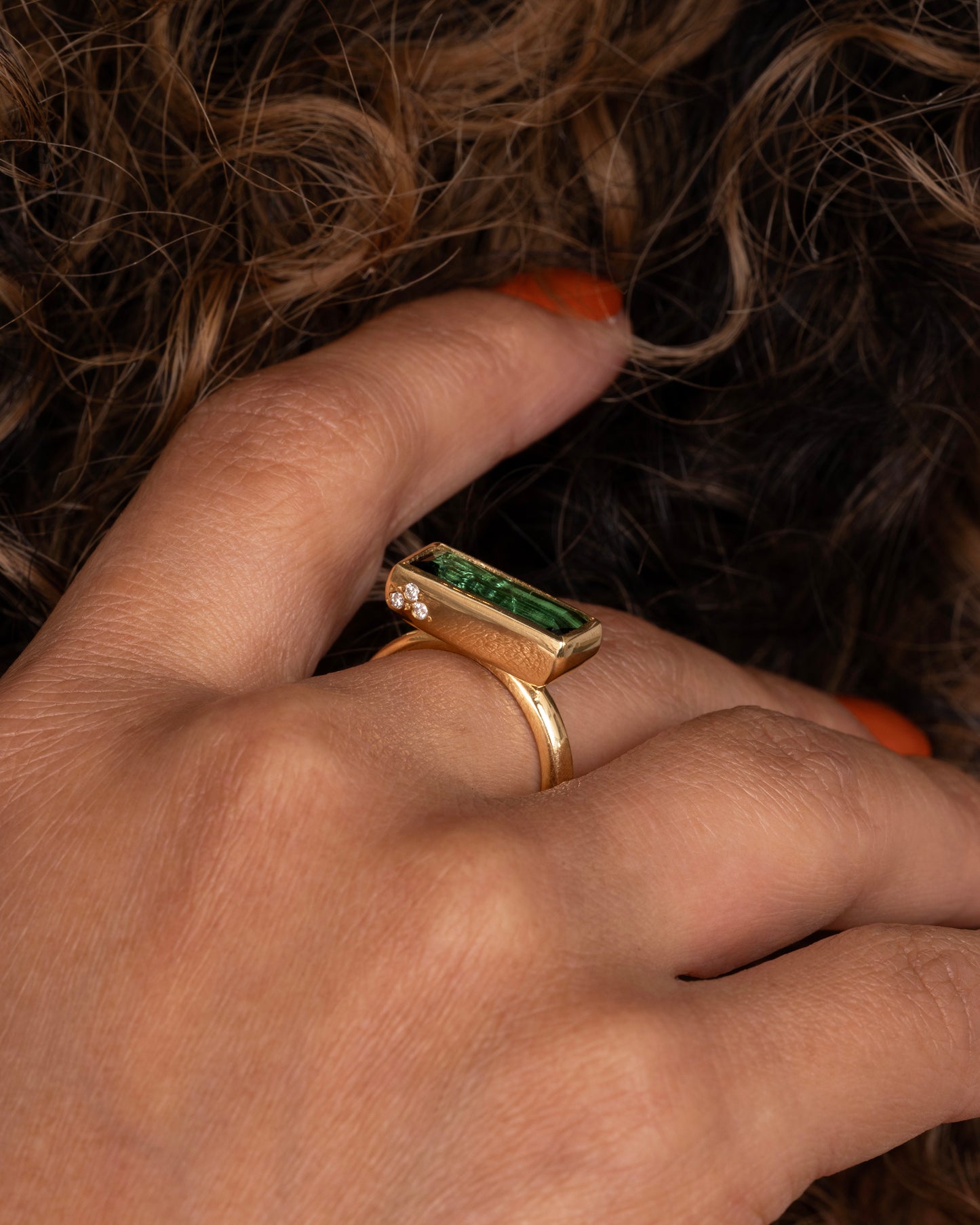 A yellow gold ring with a baguette indicolite tourmaline and small white diamonds. Shown on a hand.