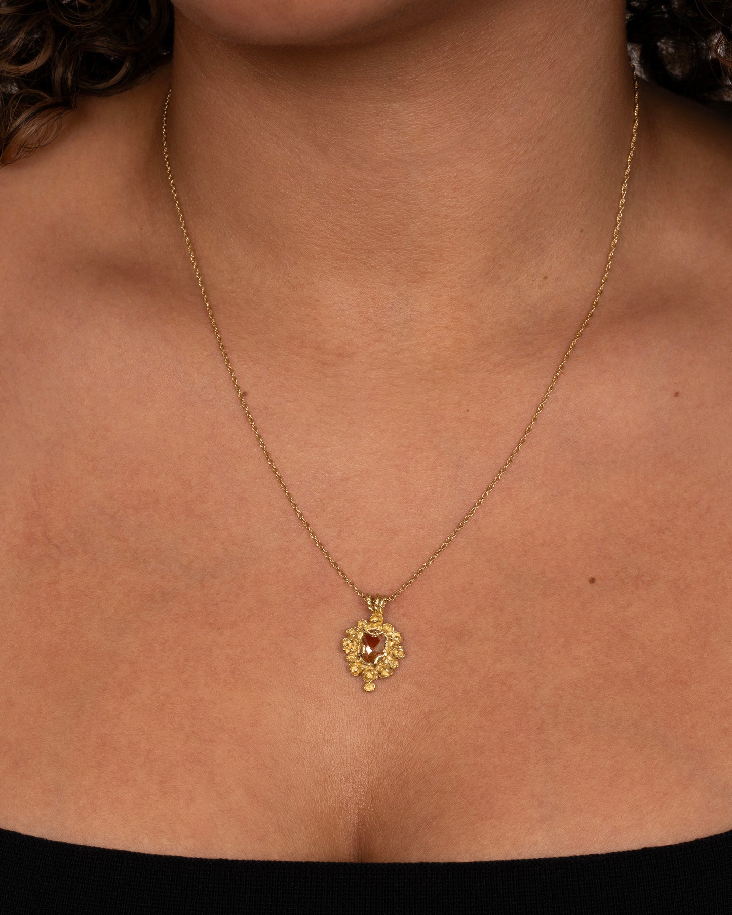 A yellow gold pendant reminiscent of an antique mirror with floral and vine details around an orange rose cut diamond. Shown worn around a neck.