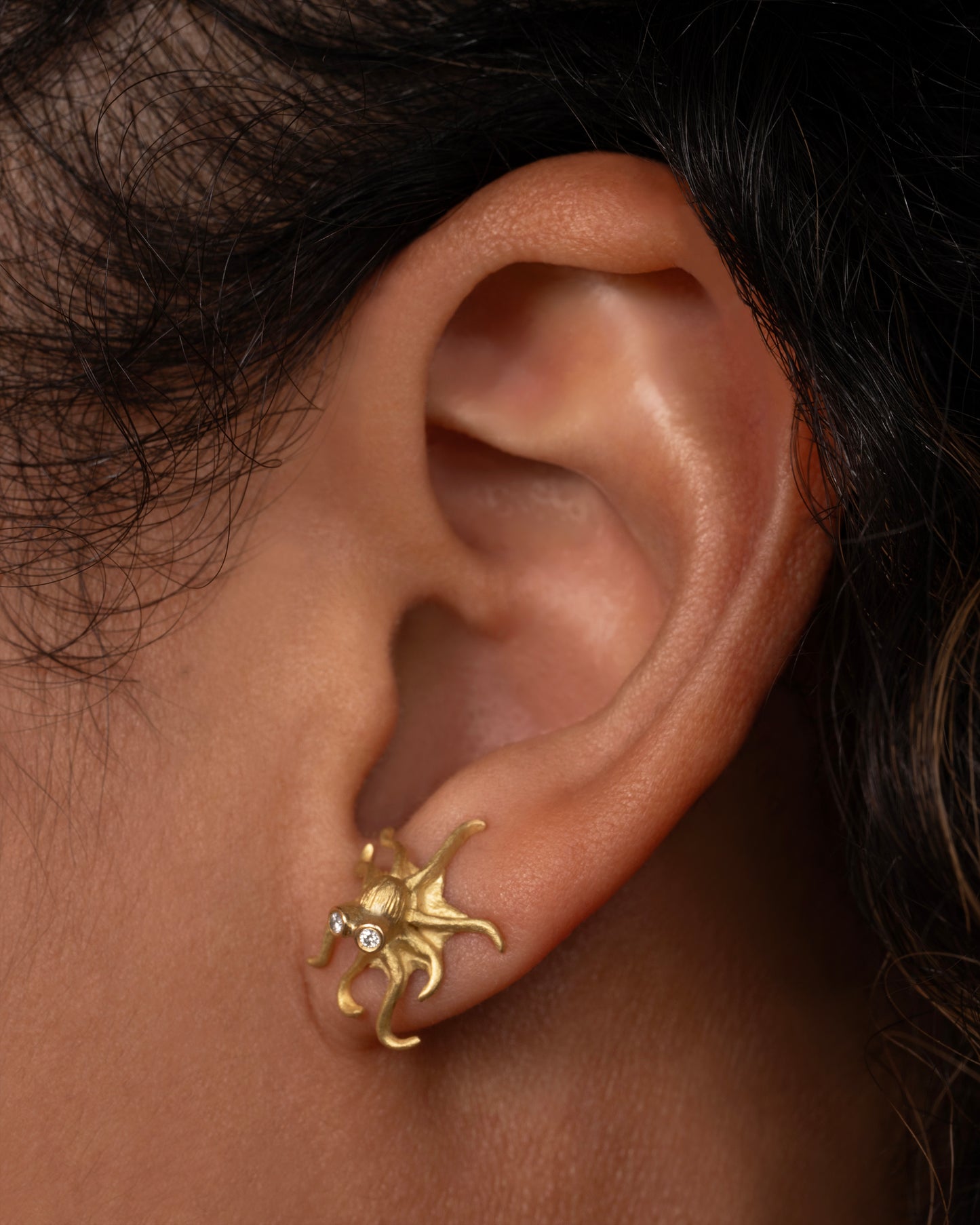 Yellow gold octopus earrings with diamond eyes. View on an ear. 