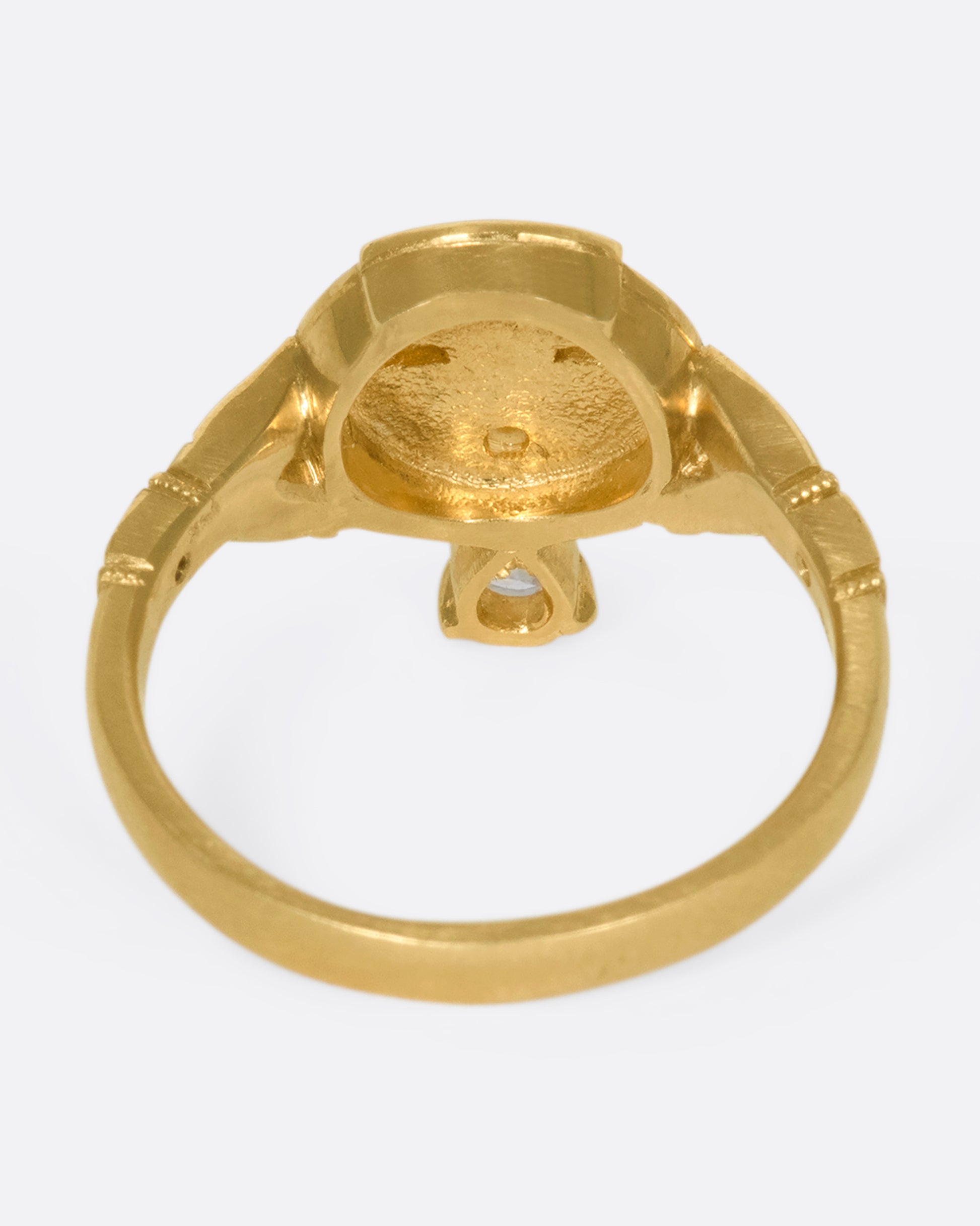 An underside view of a gold ring with a face and a pear shaped diamond tongue.