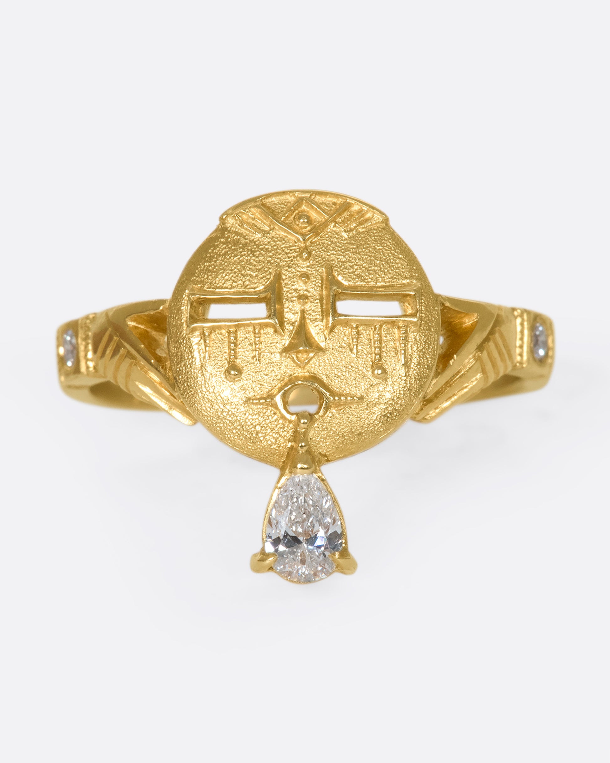A close up of a gold ring with a face and a pear shaped diamond tongue.
