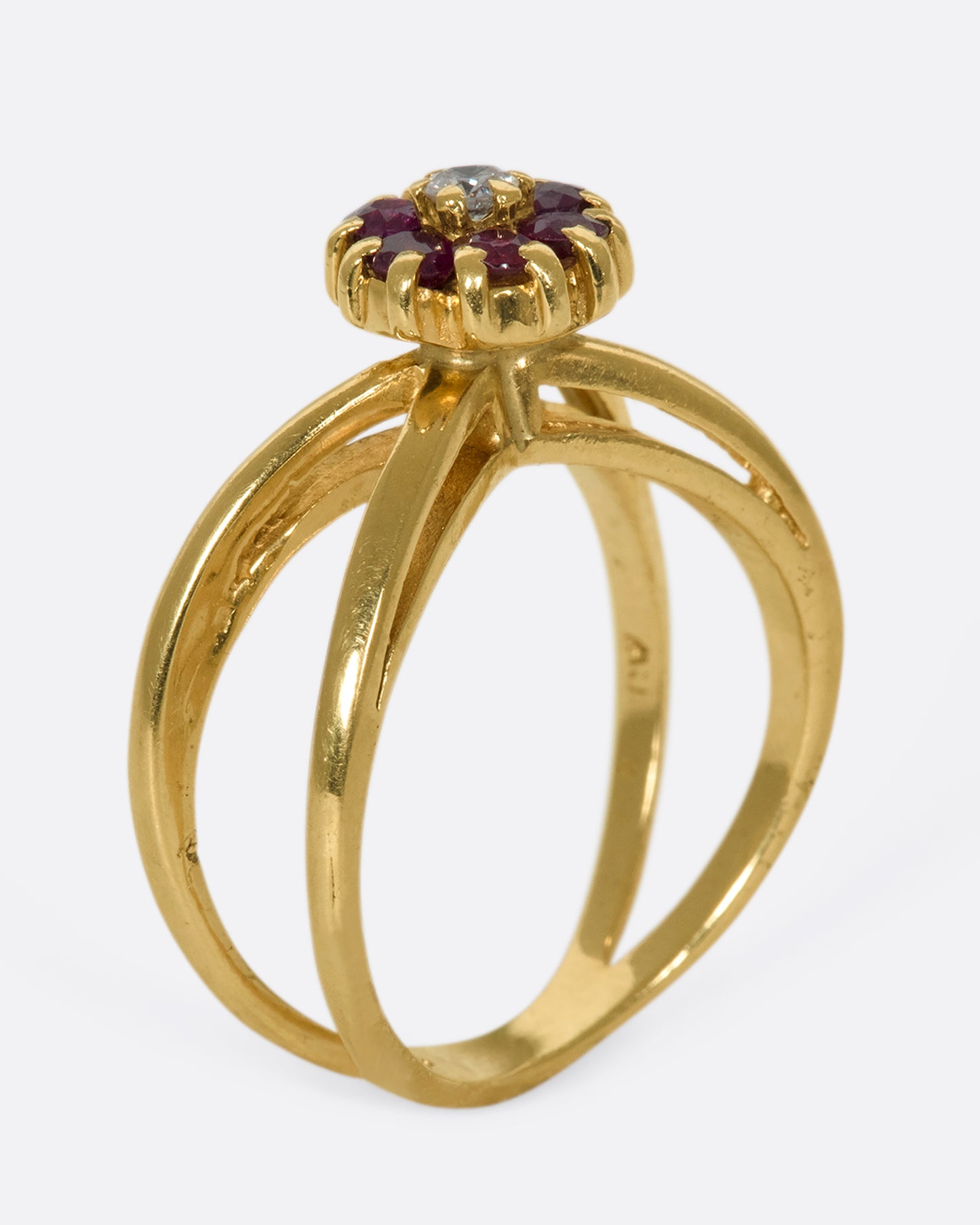 A view of a yellow gold double banded ring with a ruby and diamond flower in the center standing up on its band.