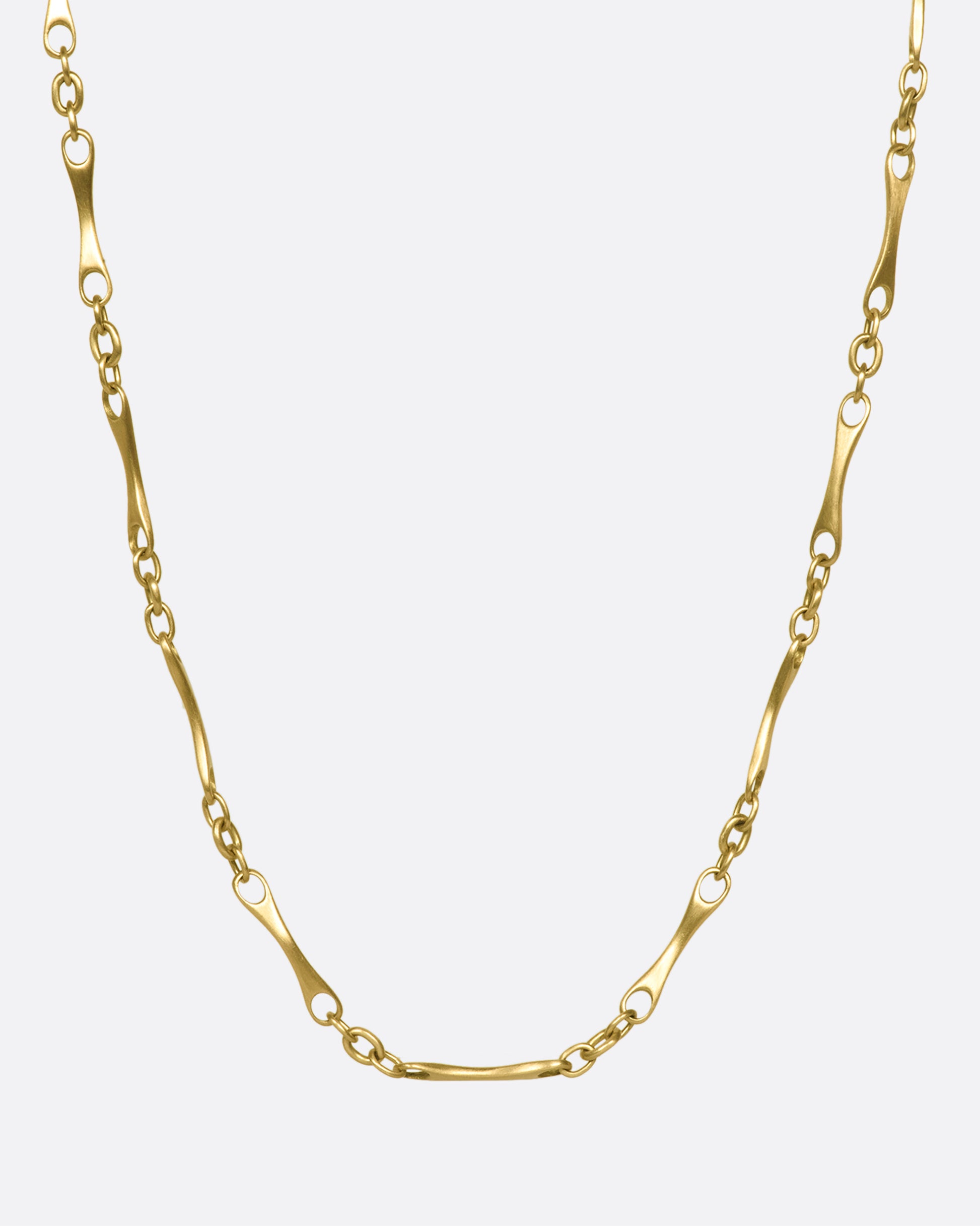 A gold necklace with elongated links with circular cut outs on each end.