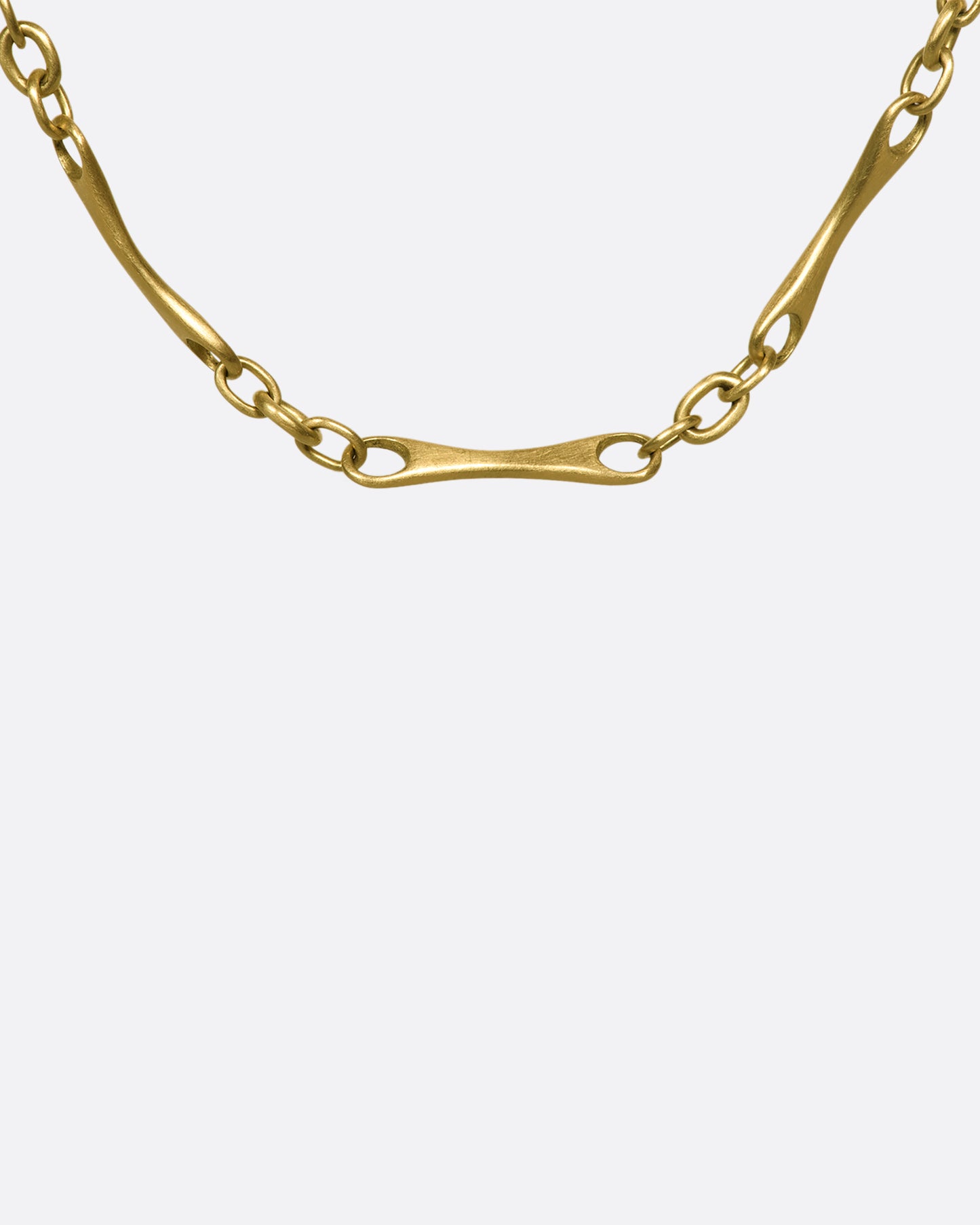 A close up of a section of a gold necklace with elongated links with circular cut outs on each end.