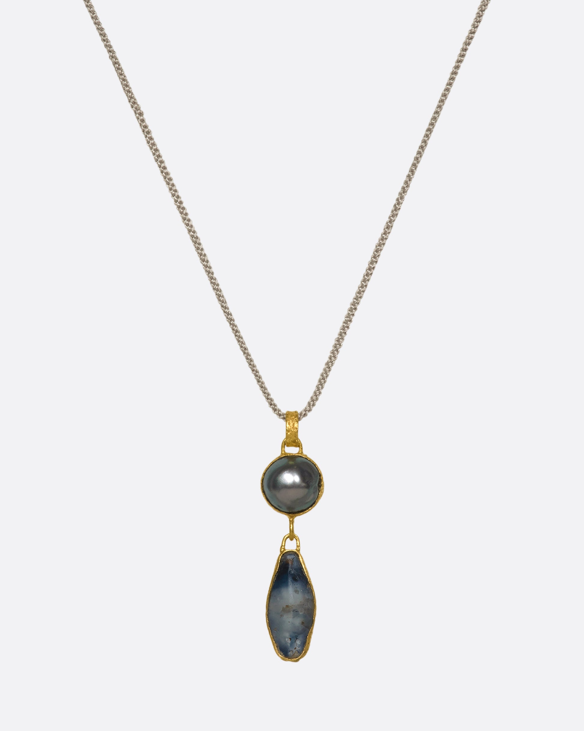 A hanging yellow gold pendant with a pearl and Sri Lankan sapphire on a cord.