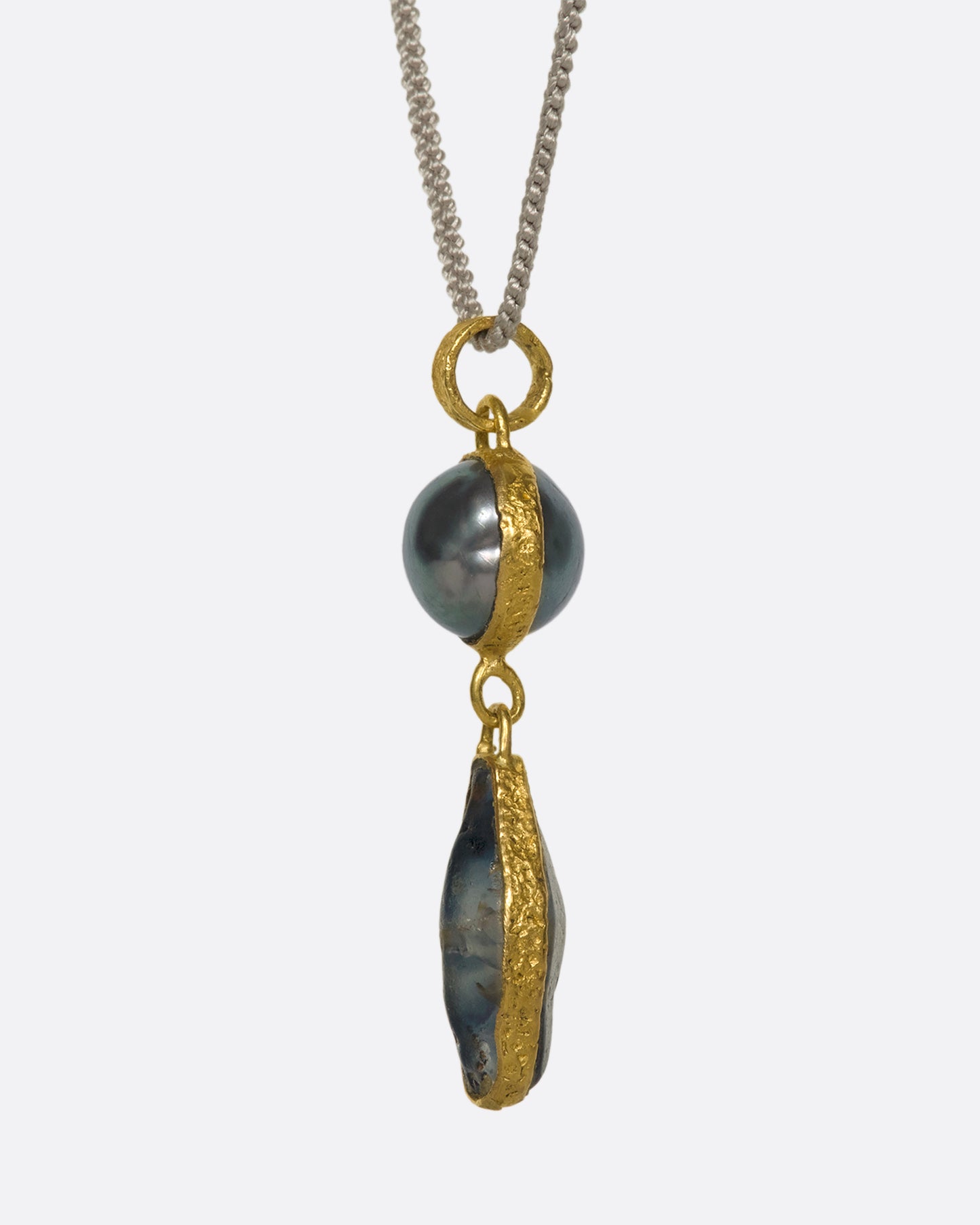 A close up of a yellow gold pendant with a pearl and Sri Lankan sapphire on a cord.