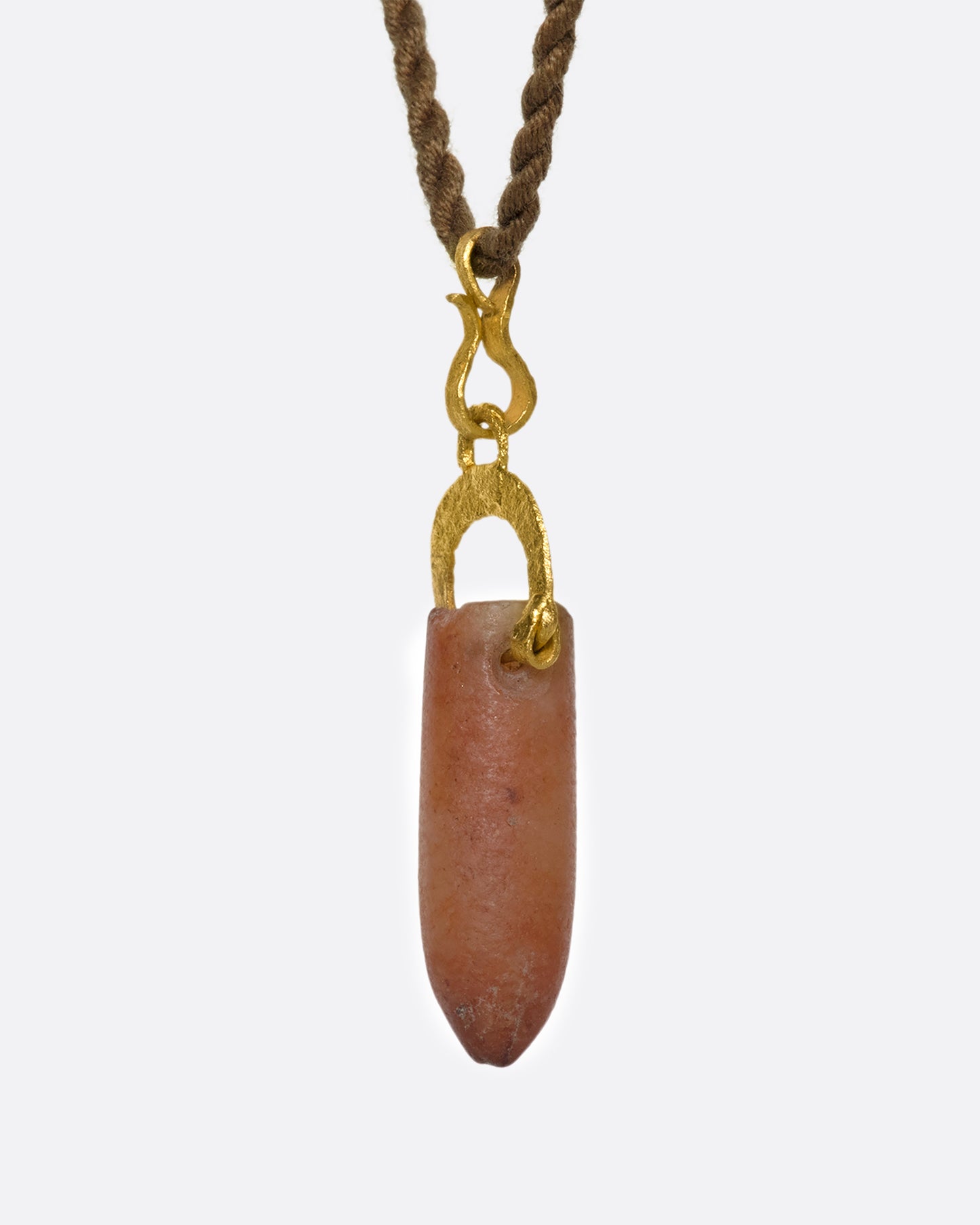 A stunning pre-Columbian carnelian bullet pendant suspended in 22k gold from a lengthy, twisted brown chord