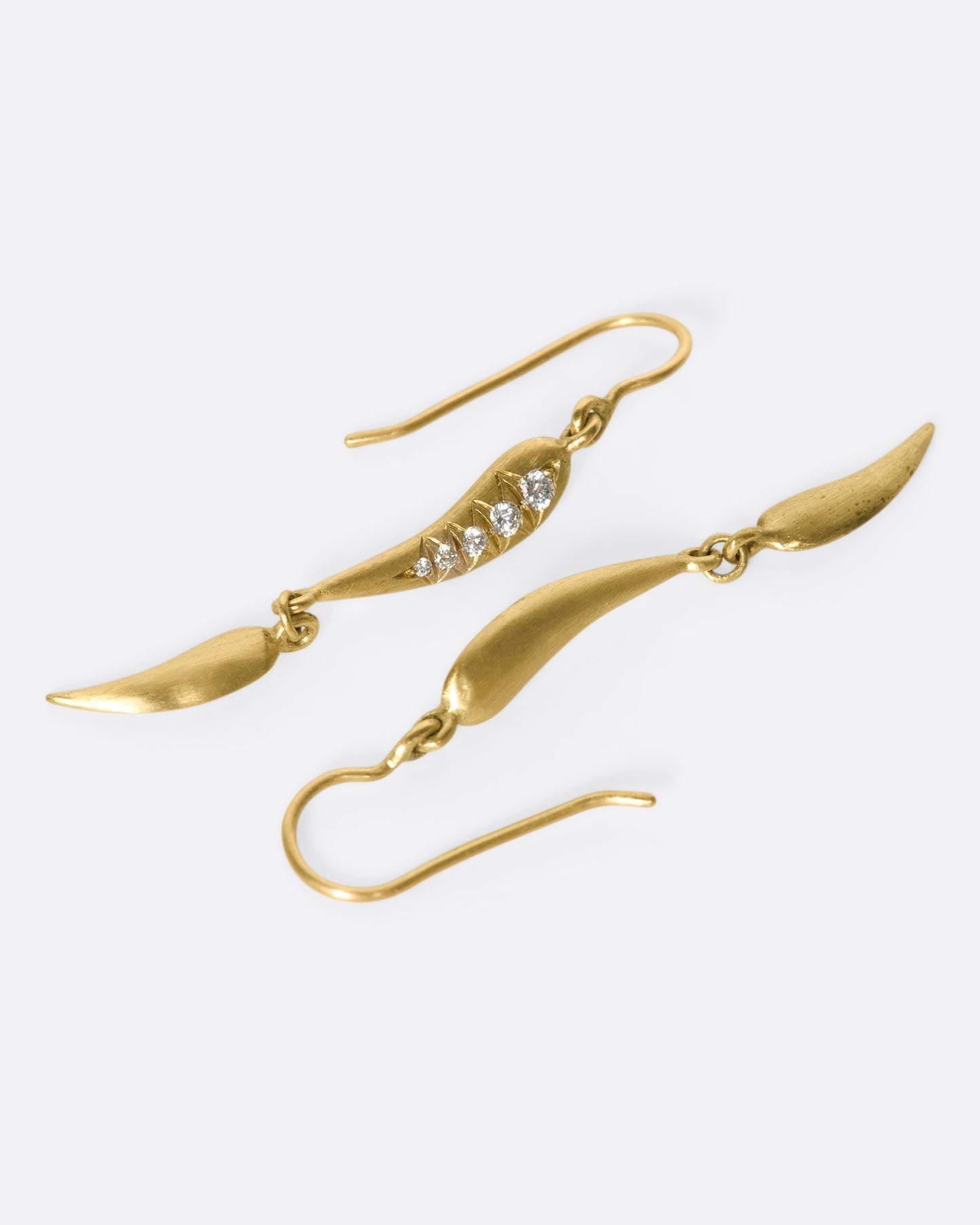 A photo of laying down gold drop earrings with 2 curved segments on each side, two of which have 5 diamonds.