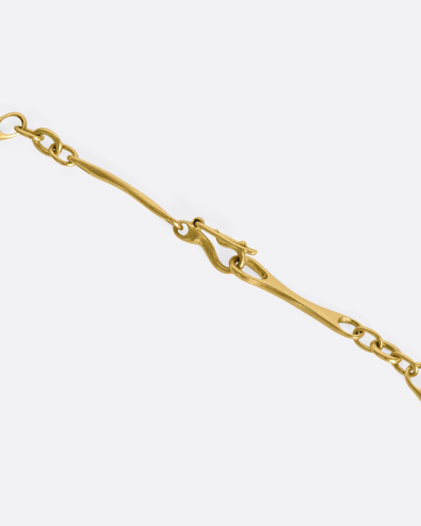 A close up of the clasp of a gold necklace with elongated links with circular cut outs on each end.