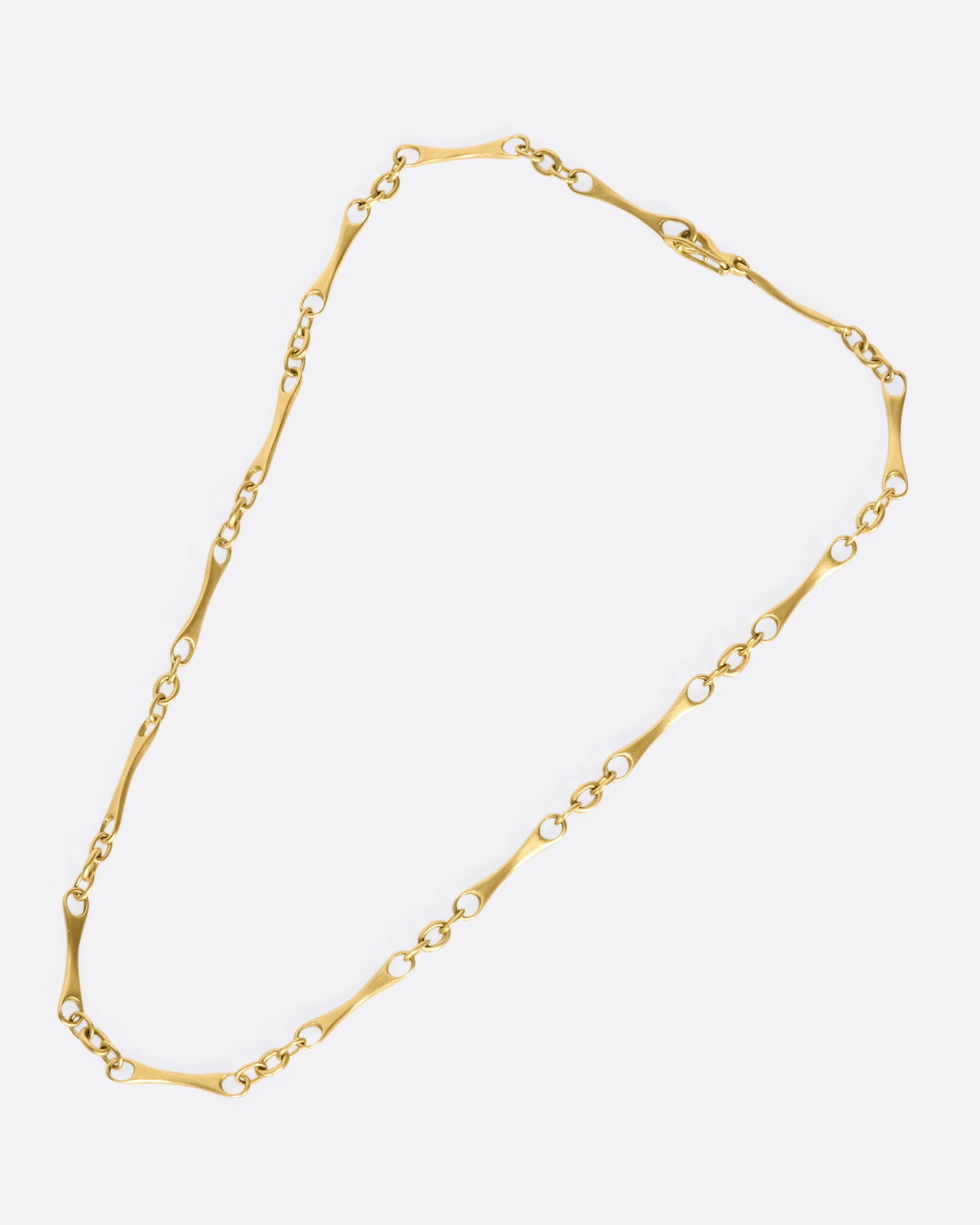 A gold necklace with elongated links with circular cut outs on each end. laying down flat.