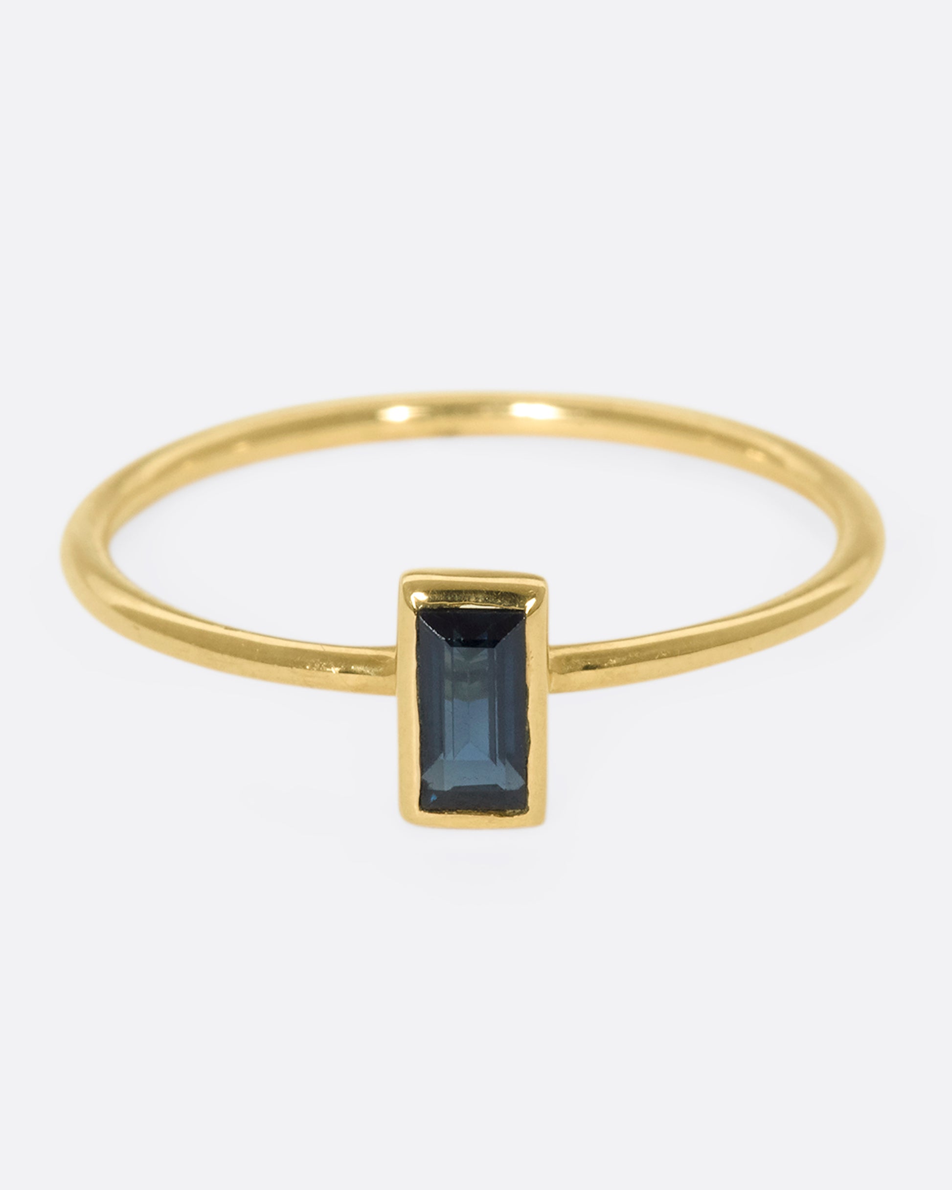 A 9k gold stacking ring with a vertical, bezel-set blue sapphire baguette