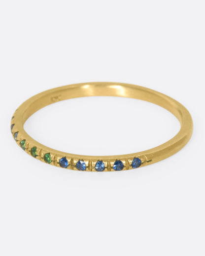 A thin yellow gold band with three green garnets set in the middle and five blue sapphires on either side. Shown from the side.