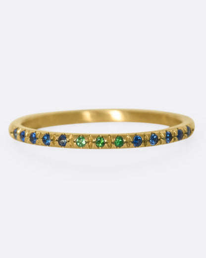 A thin yellow gold band with three green garnets set in the middle and five blue sapphires on either side. Shown from the front.