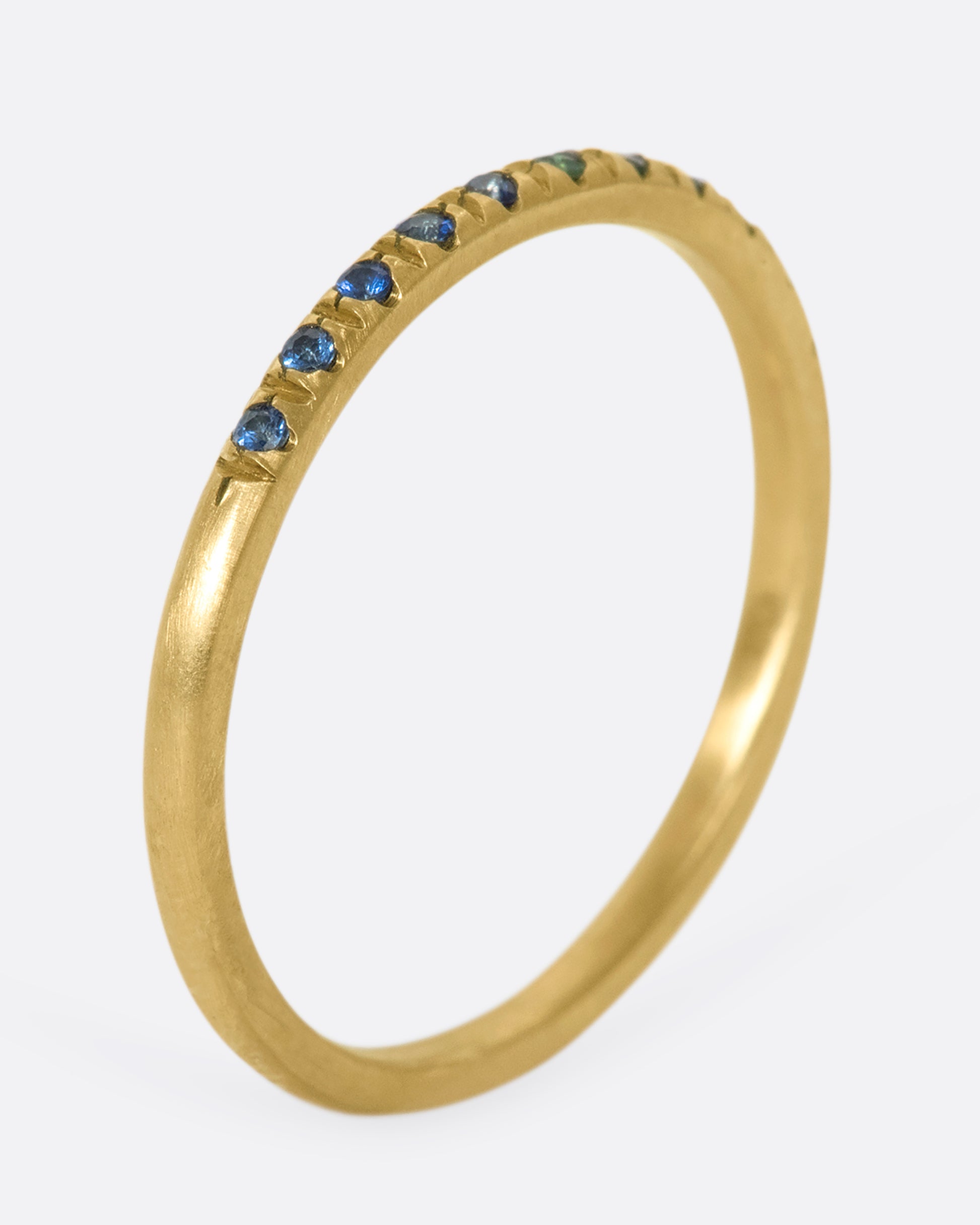 a thin yellow gold band with three green garnets in the middle and blue sapphires on either side