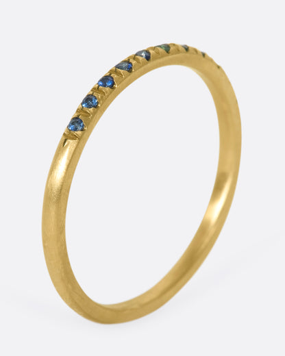 A thin yellow gold band with three green garnets set in the middle and five blue sapphires on either side. Shown standing up from the side.