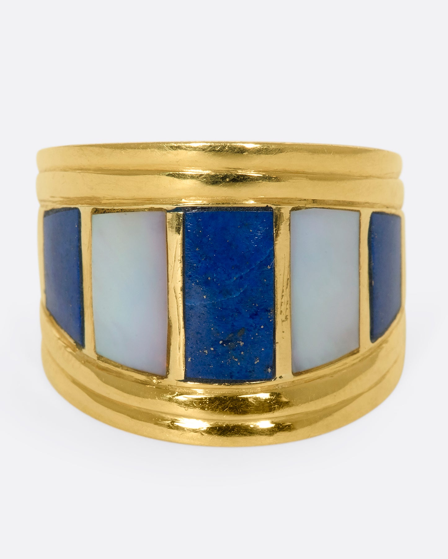 A forward view of a wide, tapered yellow gold ring with mother of pearl and lapis inlaid stripes.